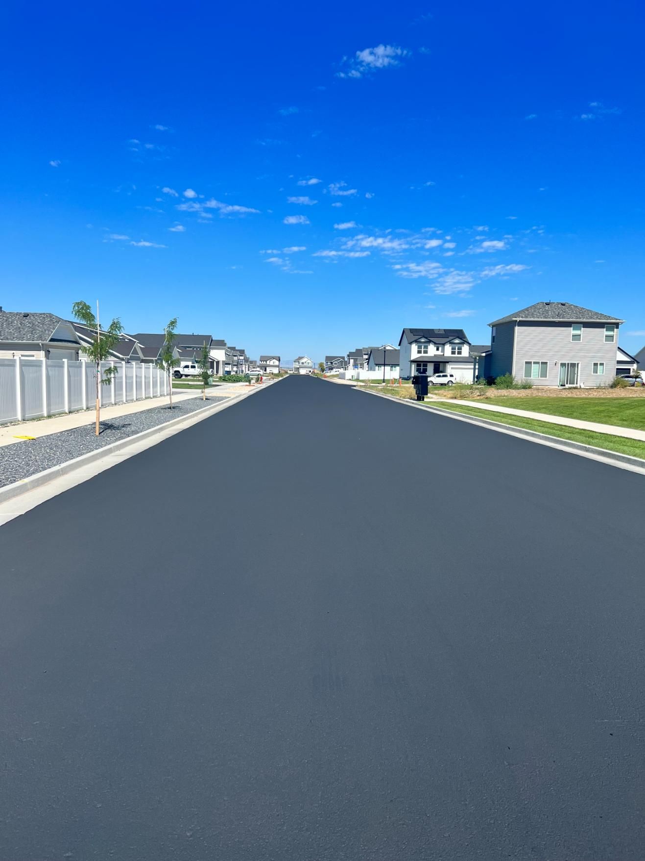 A road in a residential area with houses on both sides and a blue sky in the background.