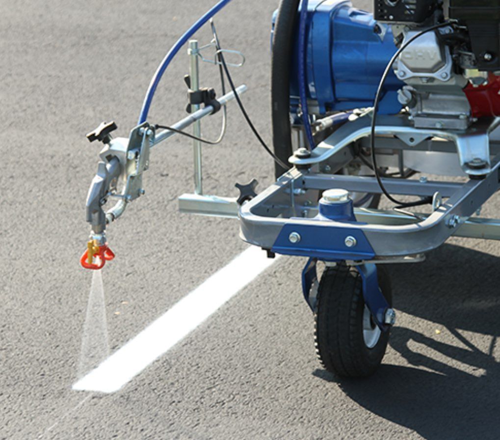 A man is kneeling down and painting a line on the ground with a brush.