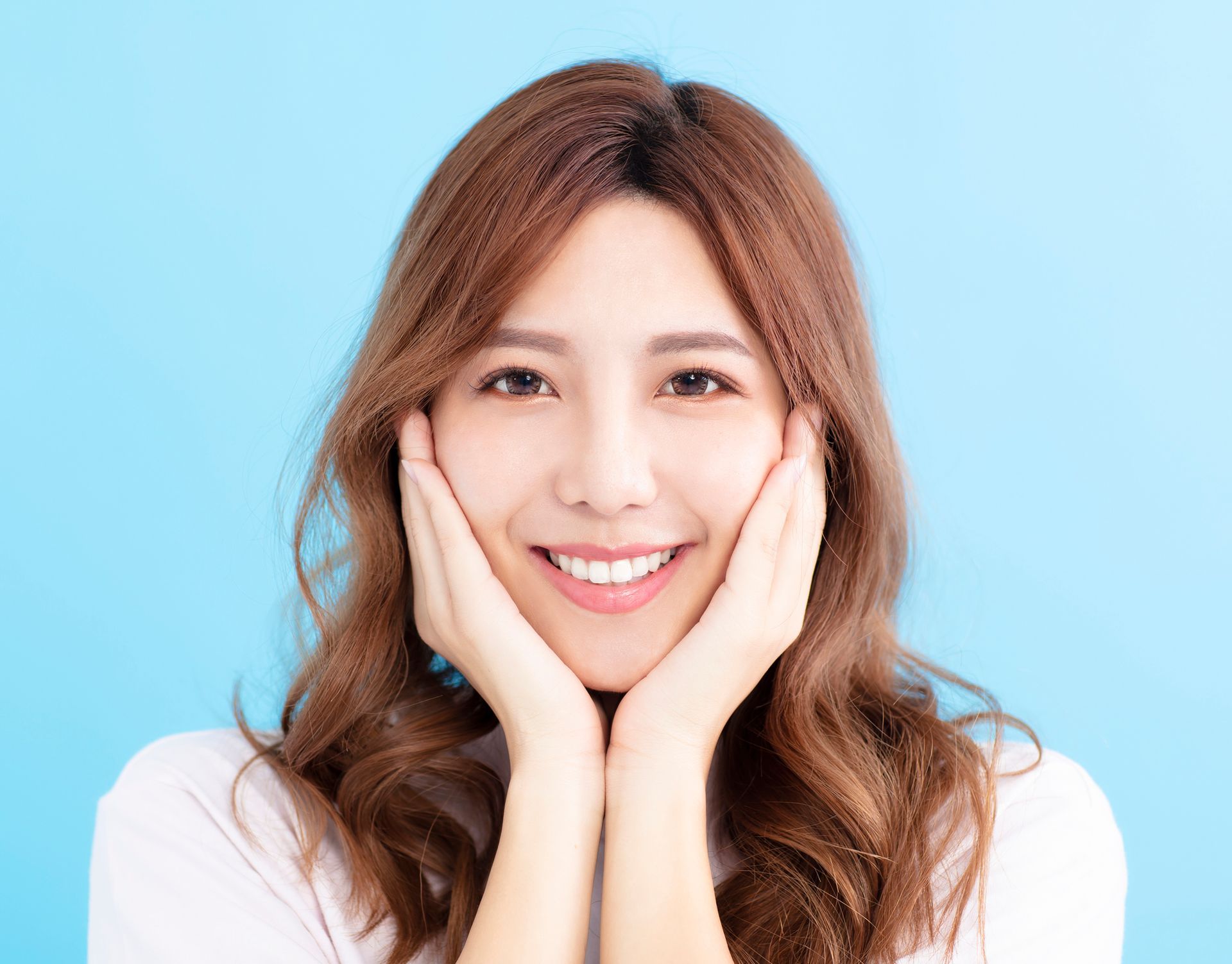 A woman is smiling with her hands on her face.