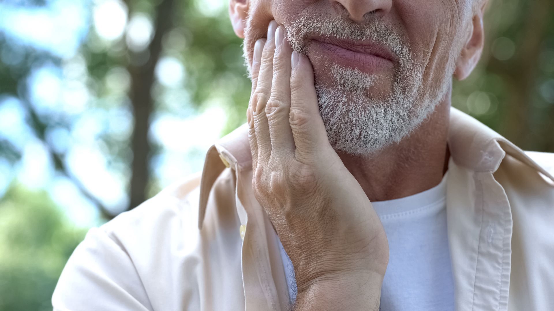 An older man with a beard is holding his hand to his chin.