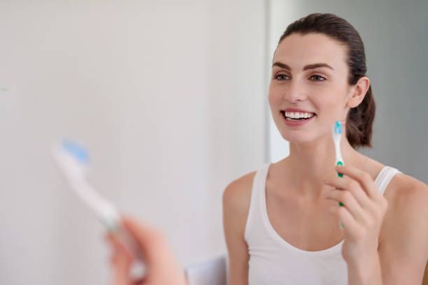 A woman is brushing her teeth in front of a mirror.