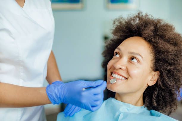 A woman is sitting in a dental chair while a dentist examines her teeth.