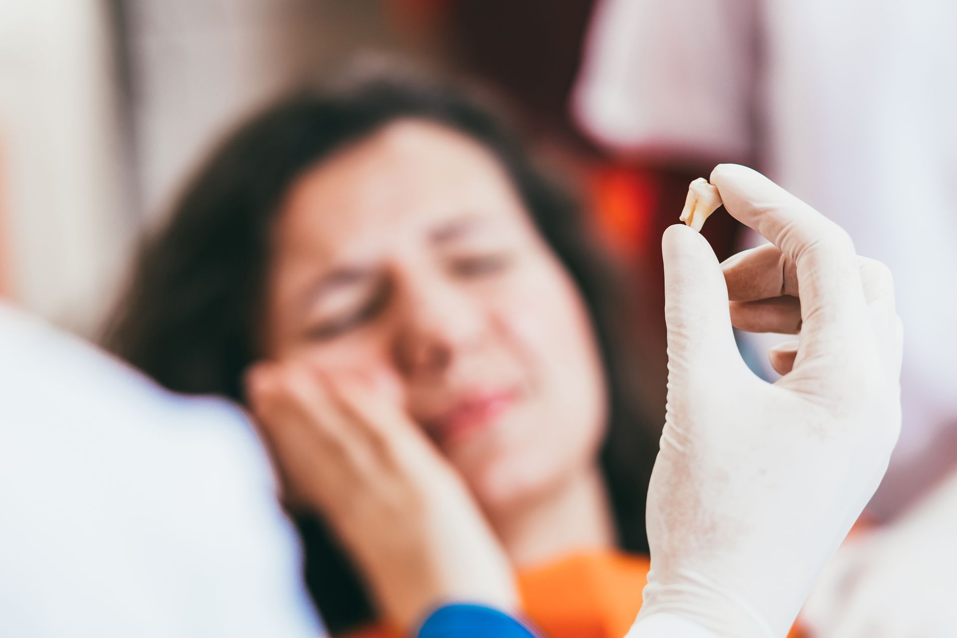 A dentist is holding a tooth in front of a woman with a toothache.