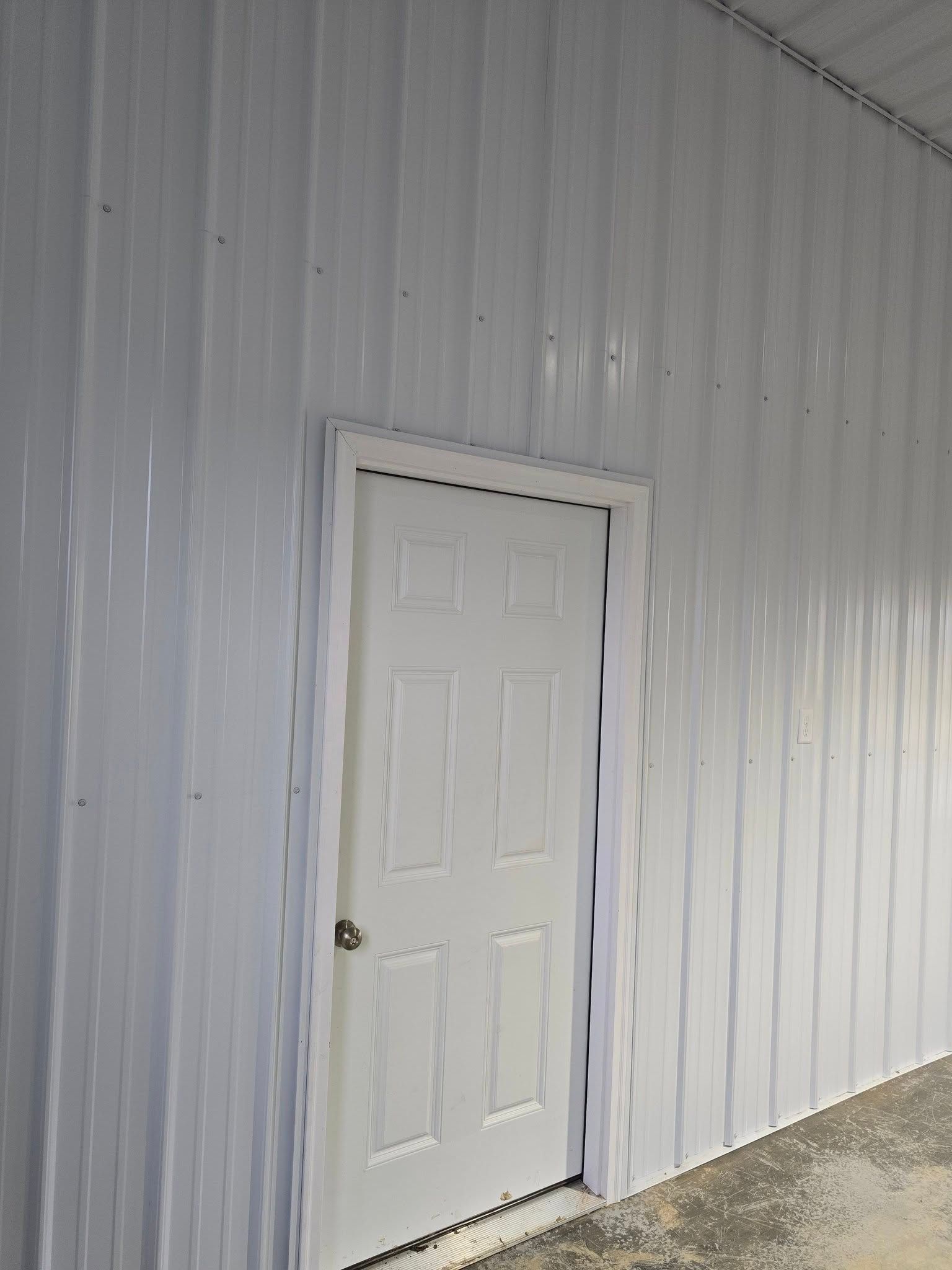 White door set in a white corrugated metal wall. Light shines on the right side.