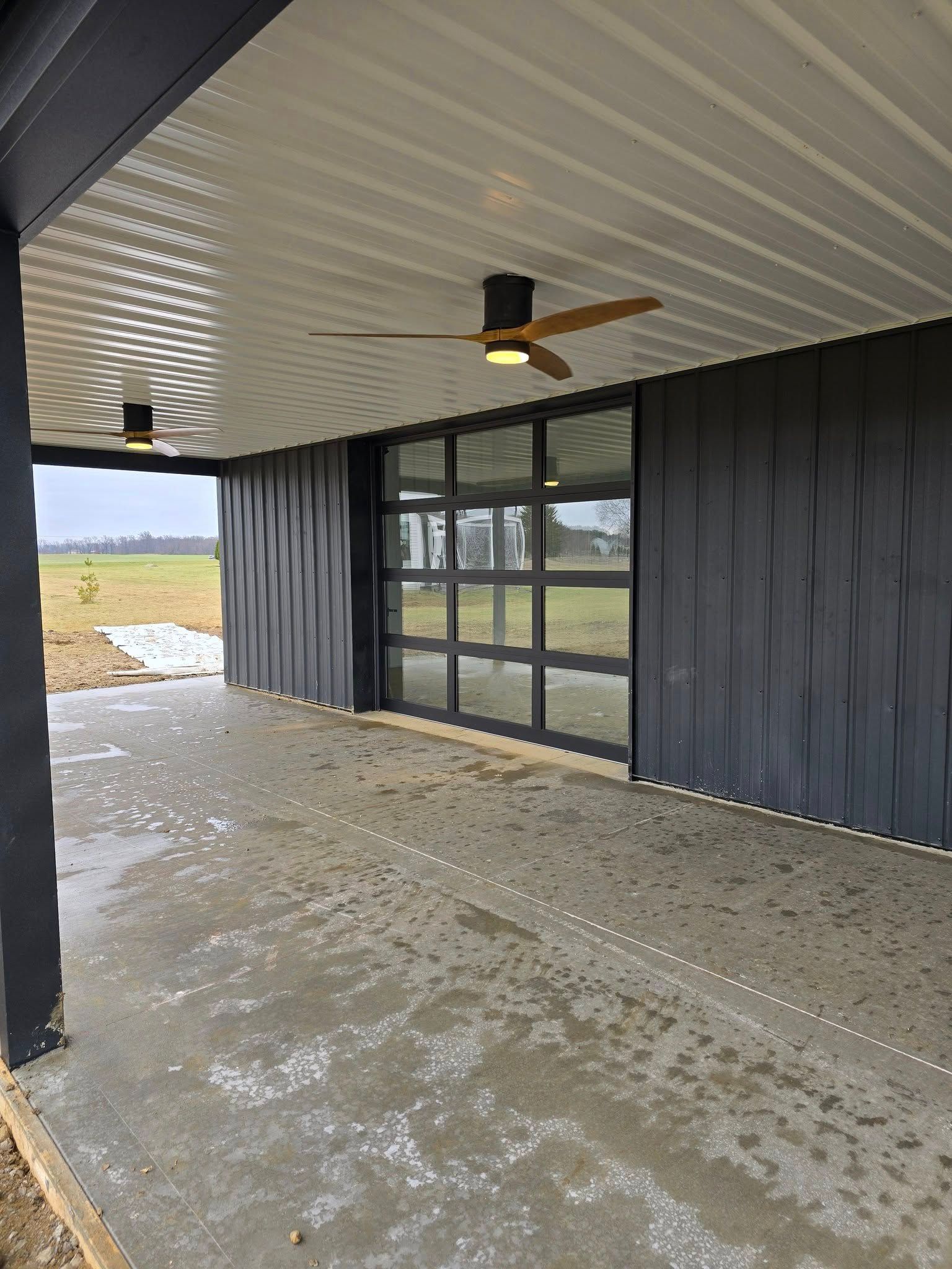 Covered outdoor patio with black siding, a glass door, and ceiling fans.
