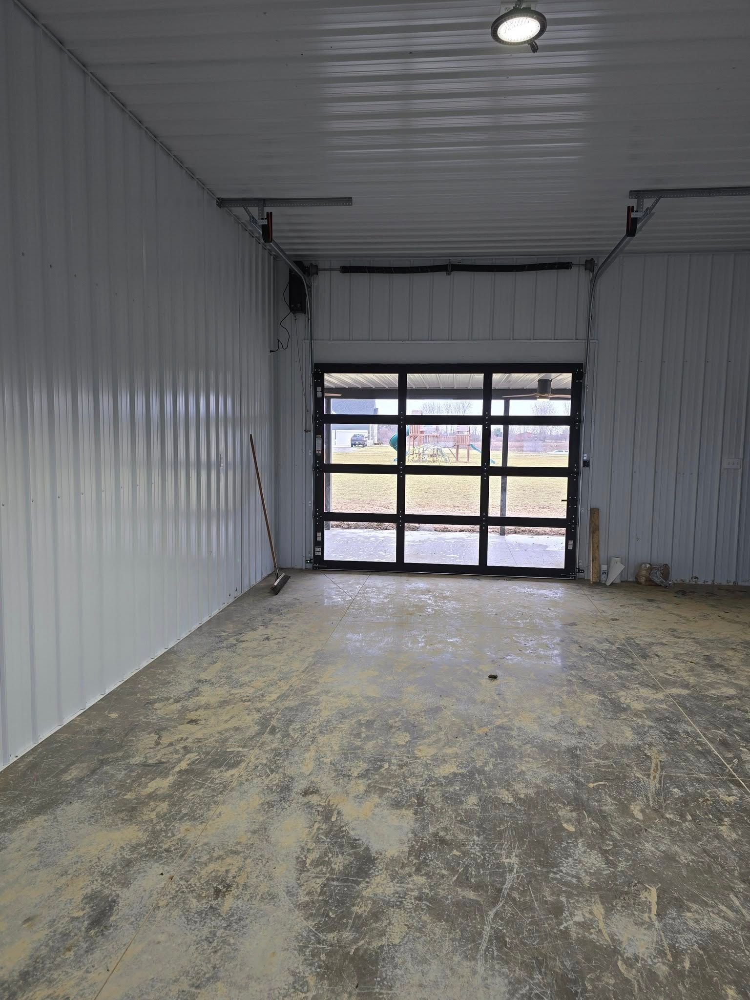 Interior of a building with a large glass door at the end, concrete floor, and white walls.
