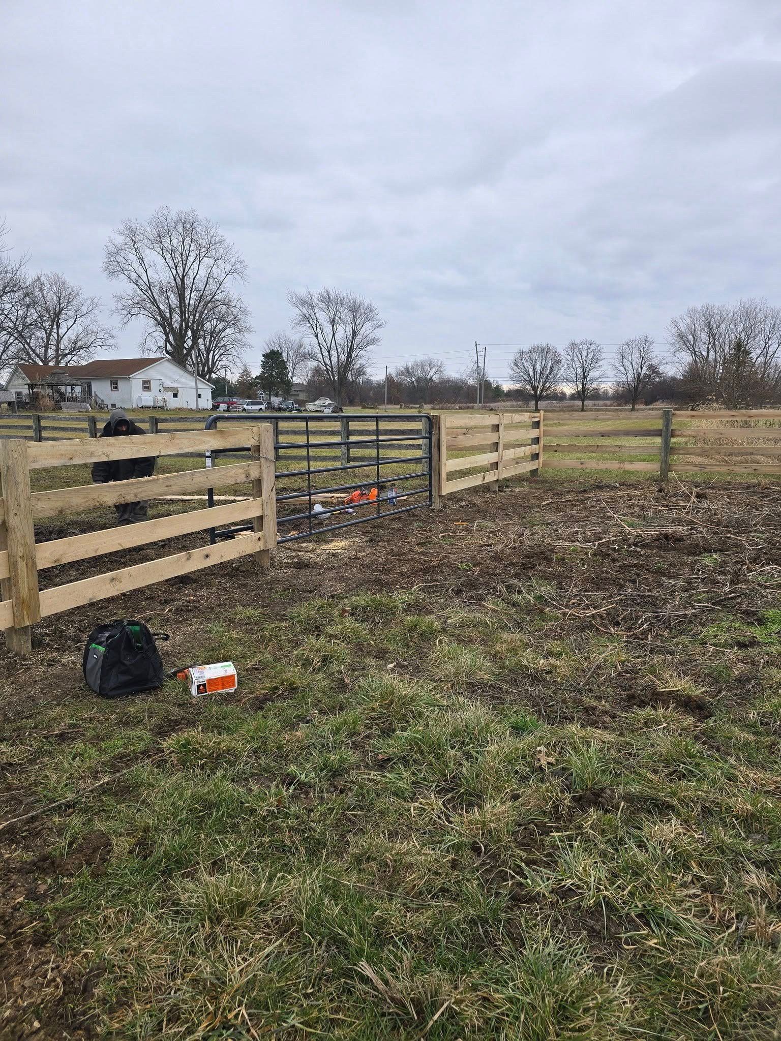 Wooden fence in a grassy field, cloudy sky, house in the background.