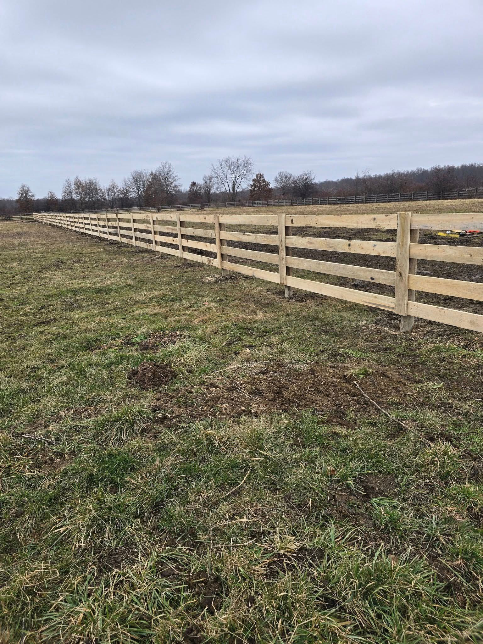 Wooden fence lines a grassy field under a cloudy sky.