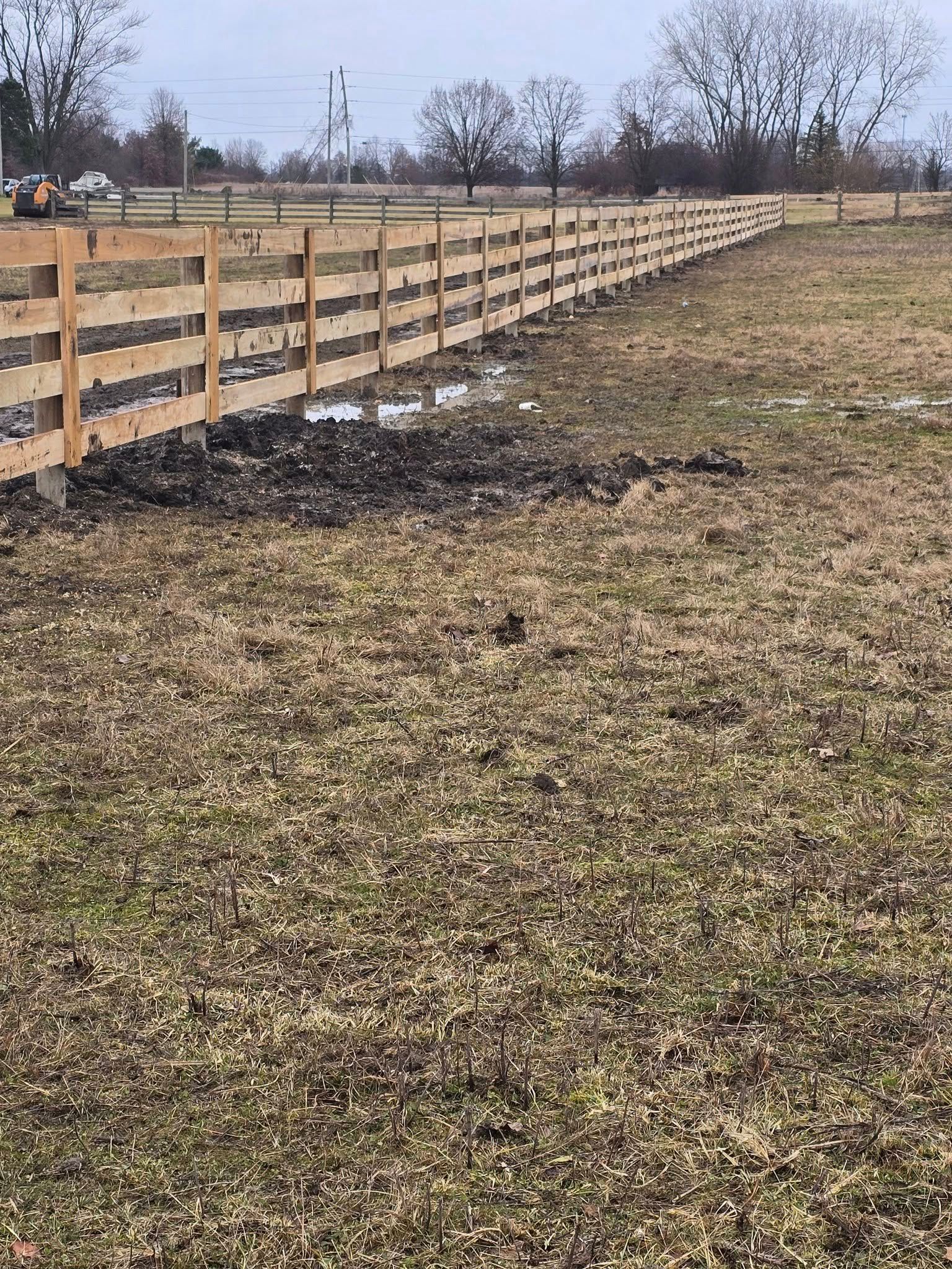 Wooden fence bordering a brown grassy field under a cloudy sky.