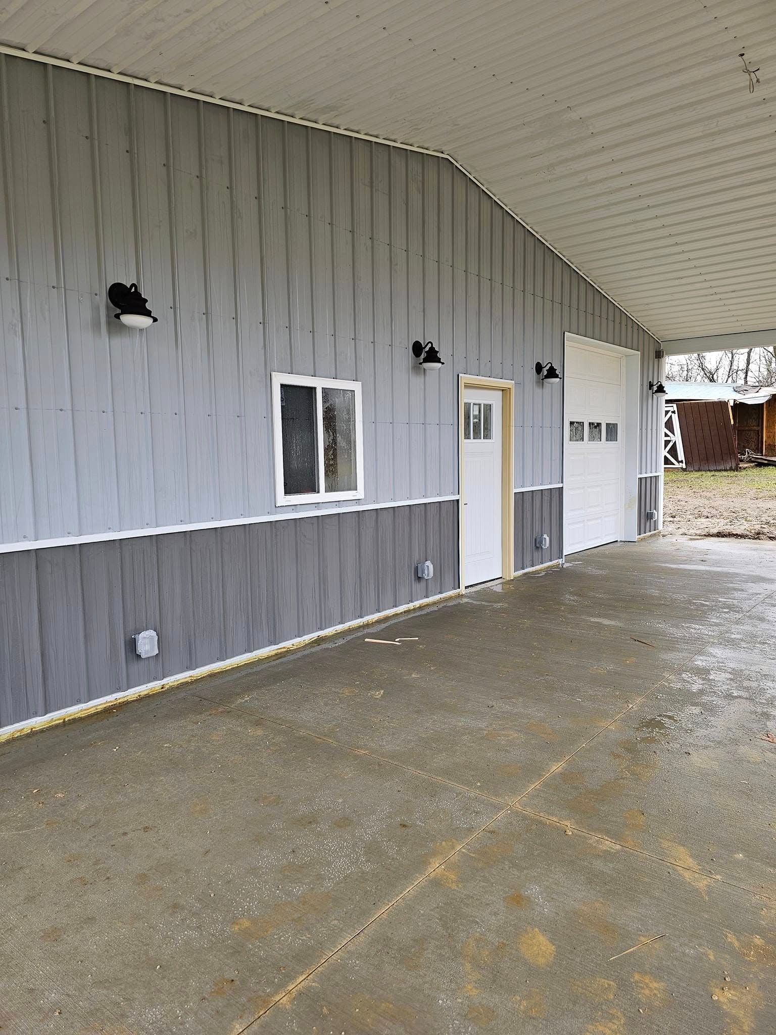 Gray and dark gray metal-sided building with a concrete floor, small windows, and a white door.