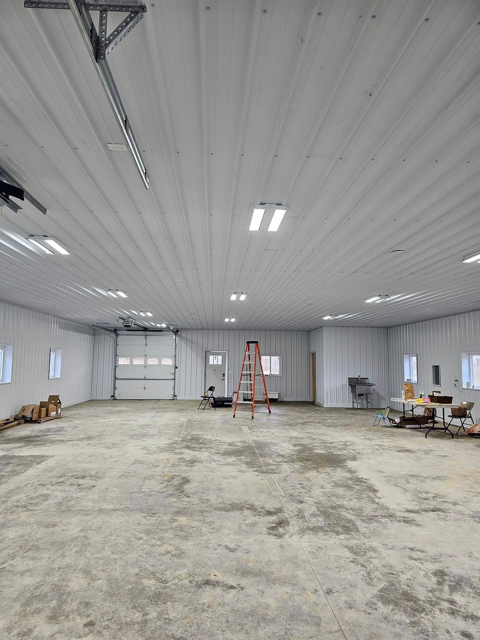 Woman stands in a large, empty white building with a concrete floor, next to an open garage door.