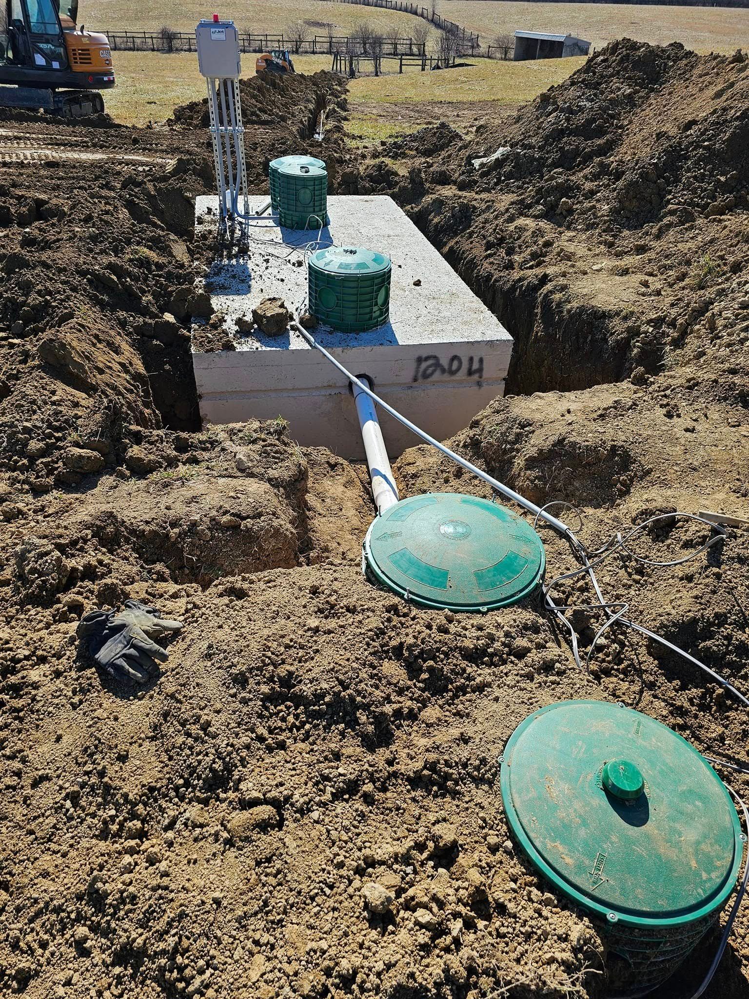 Septic system installation: Tanks, soil, and pipes in an open trench in an outdoor setting.