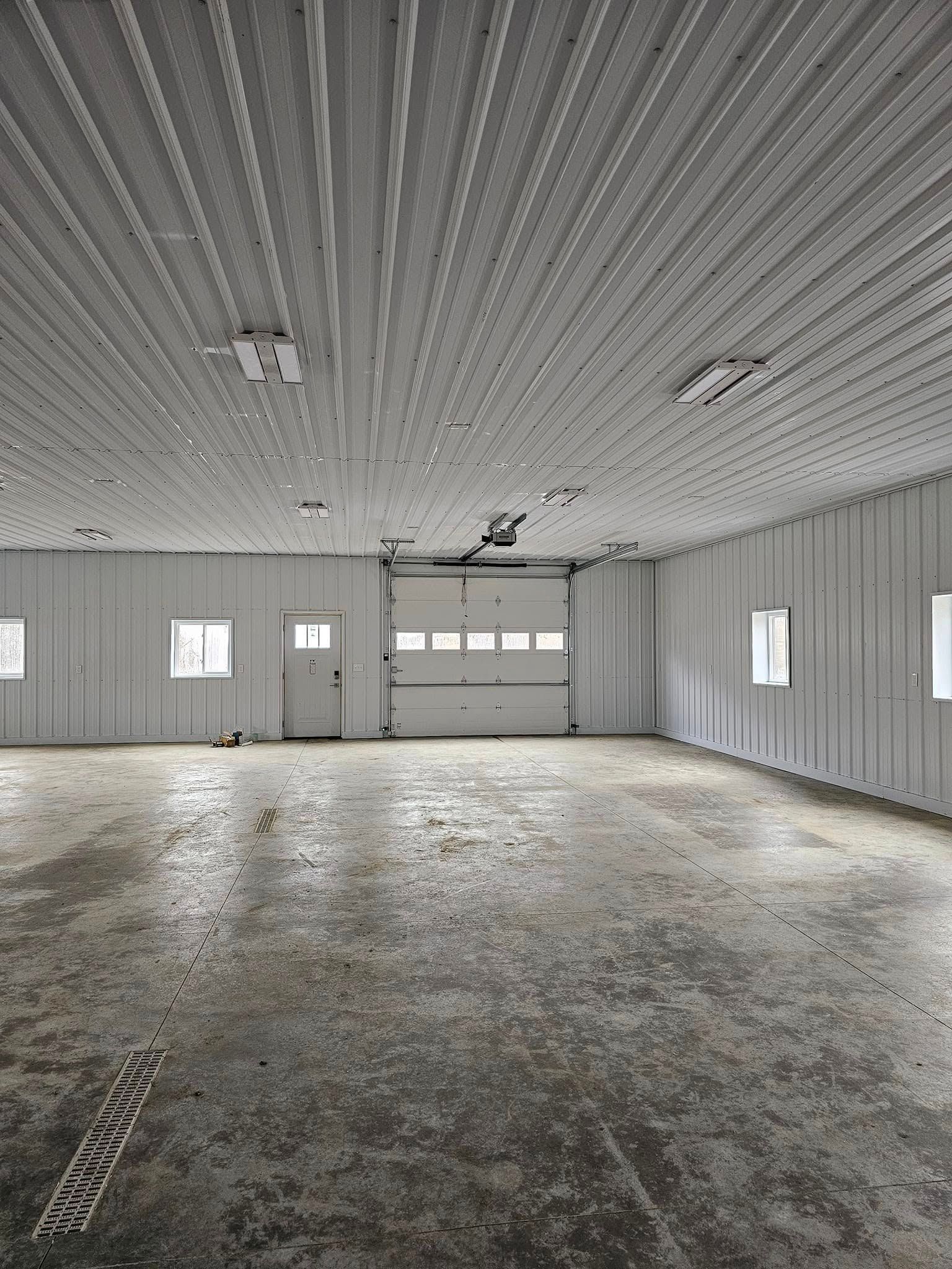 Empty white industrial space with a concrete floor, garage door, and windows.