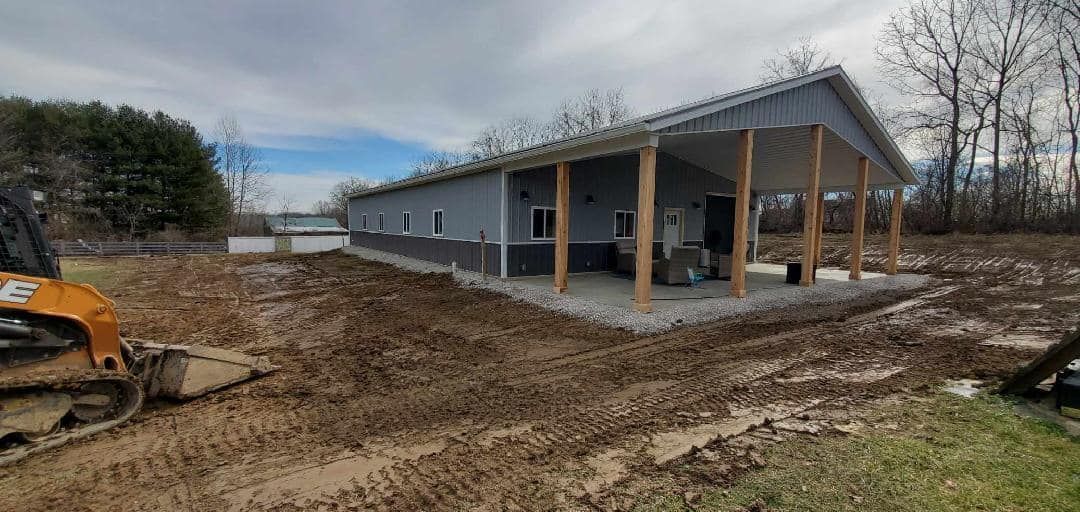 A long, gray building with a covered porch under a cloudy sky, muddy ground in front.