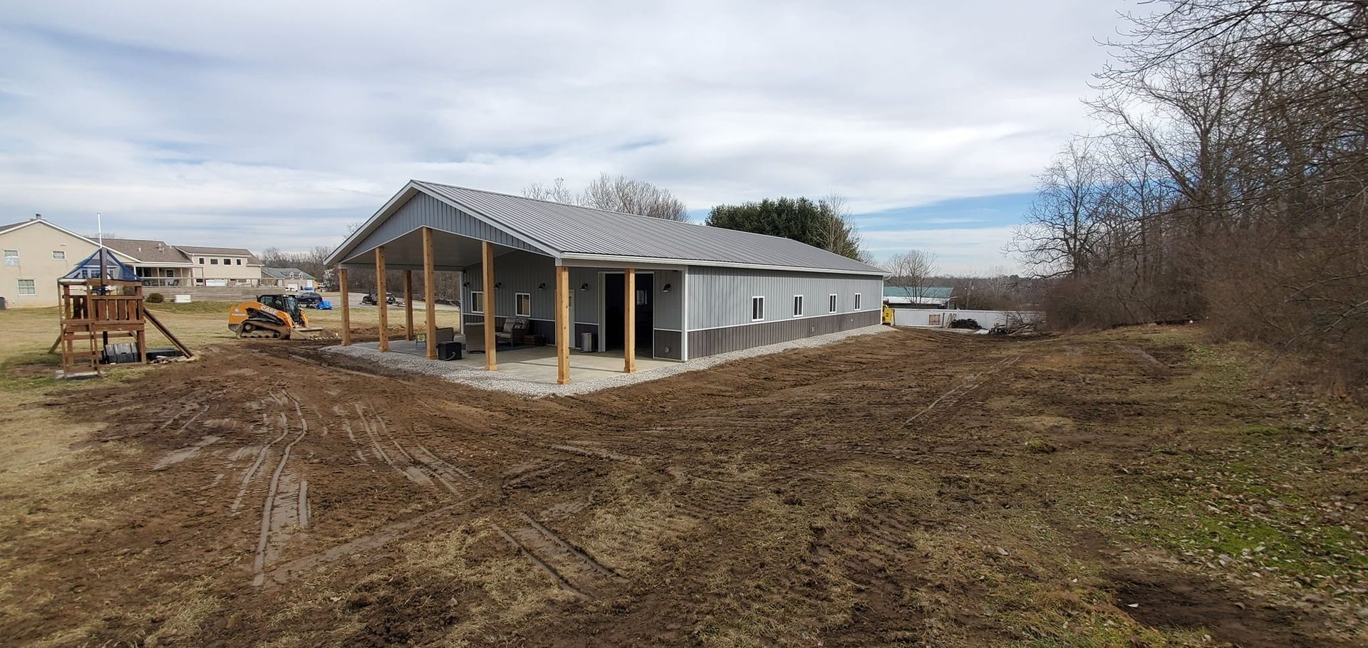 A long gray metal building with a covered patio on a brown, barren plot of land.