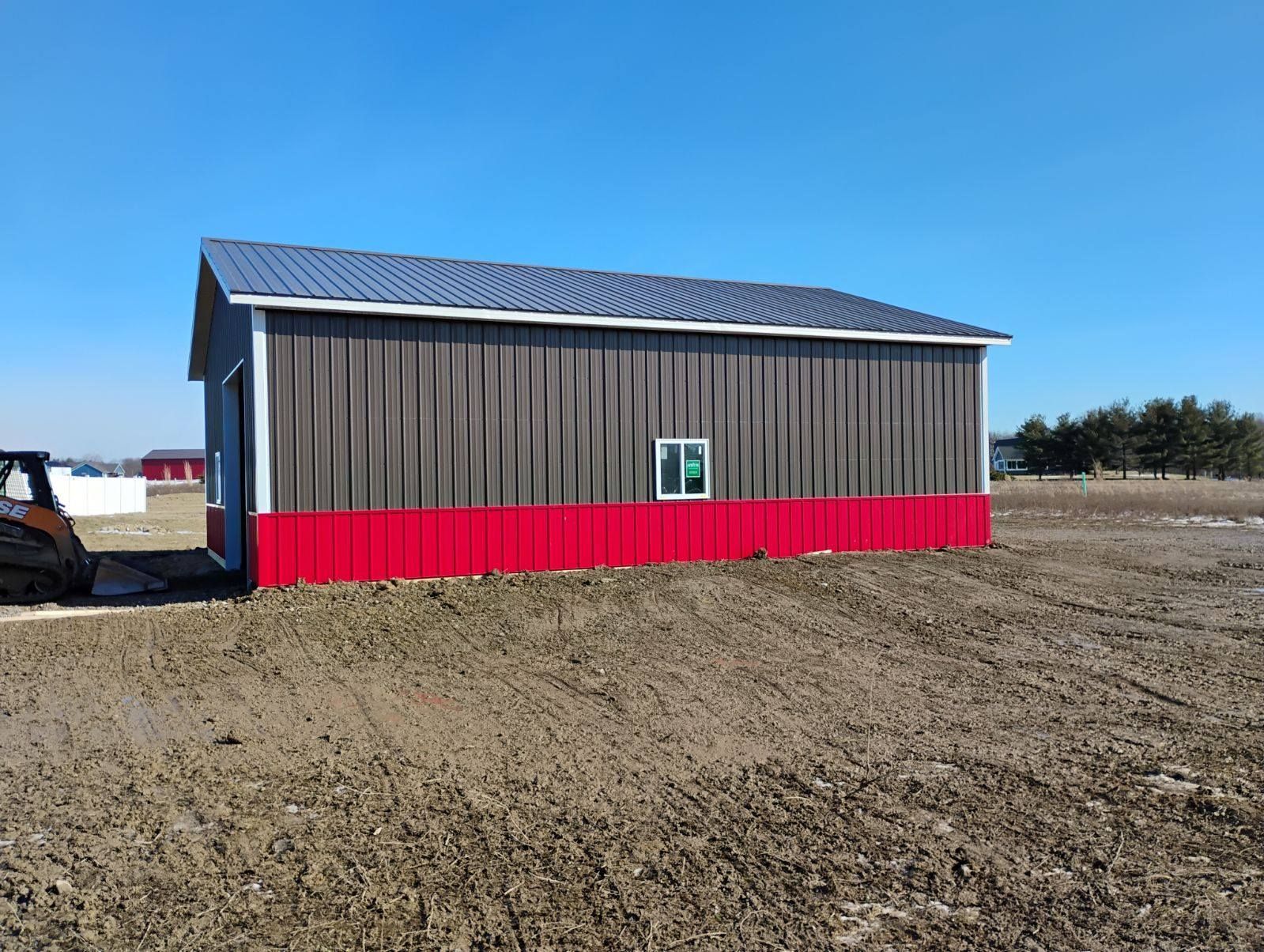 Gray and red barn on a dirt field under a clear blue sky.