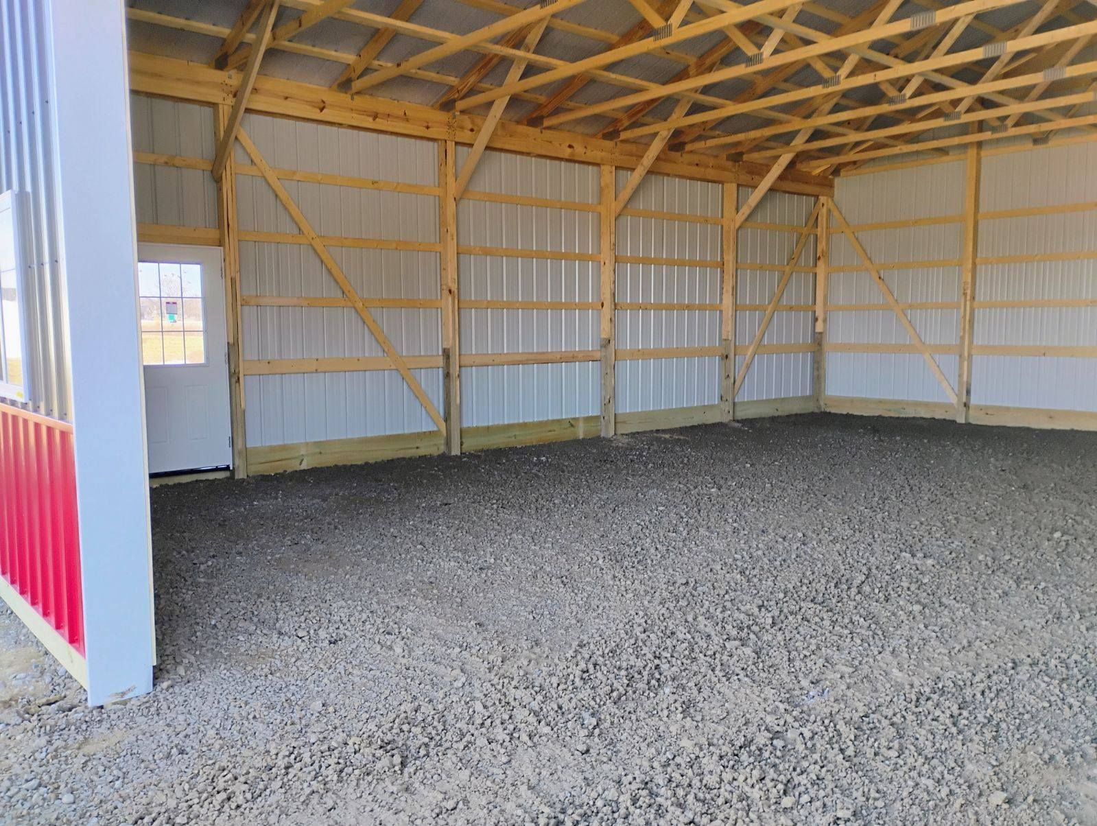 Interior of an unfinished pole barn with gravel floor, wood framing, and corrugated metal siding.
