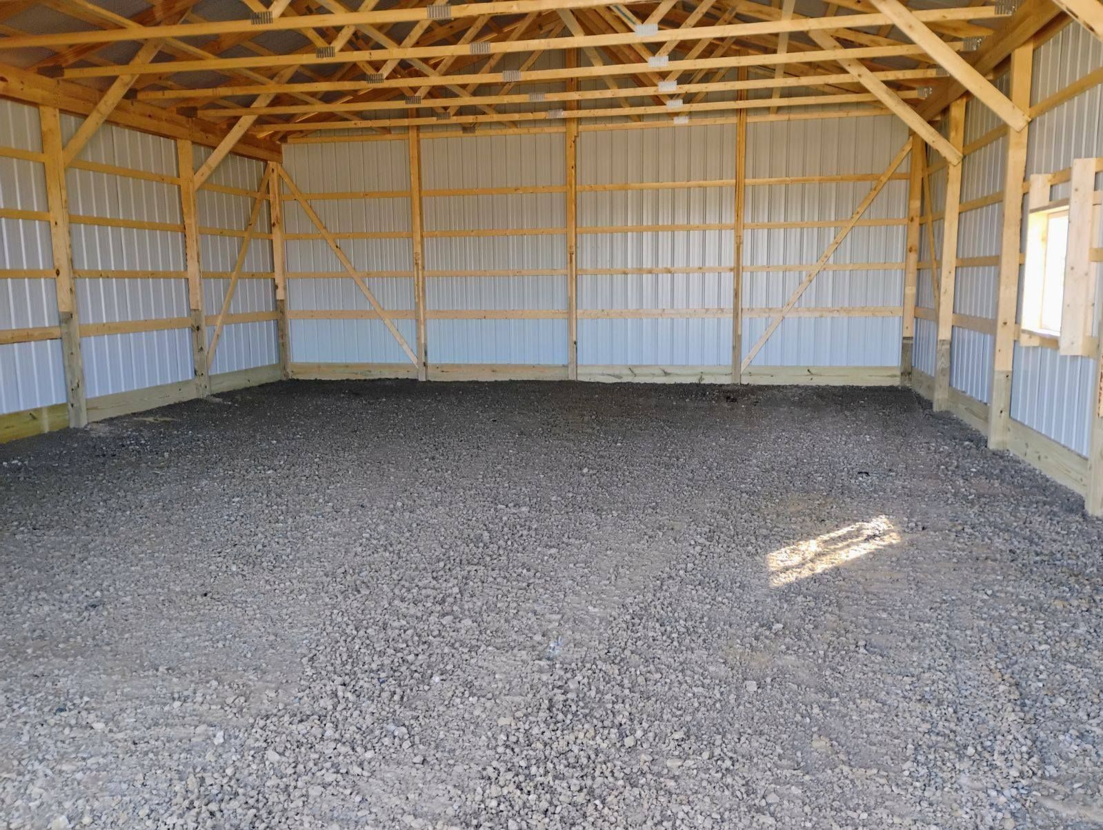 Inside of an empty, gravel-floored wooden and metal-walled barn.