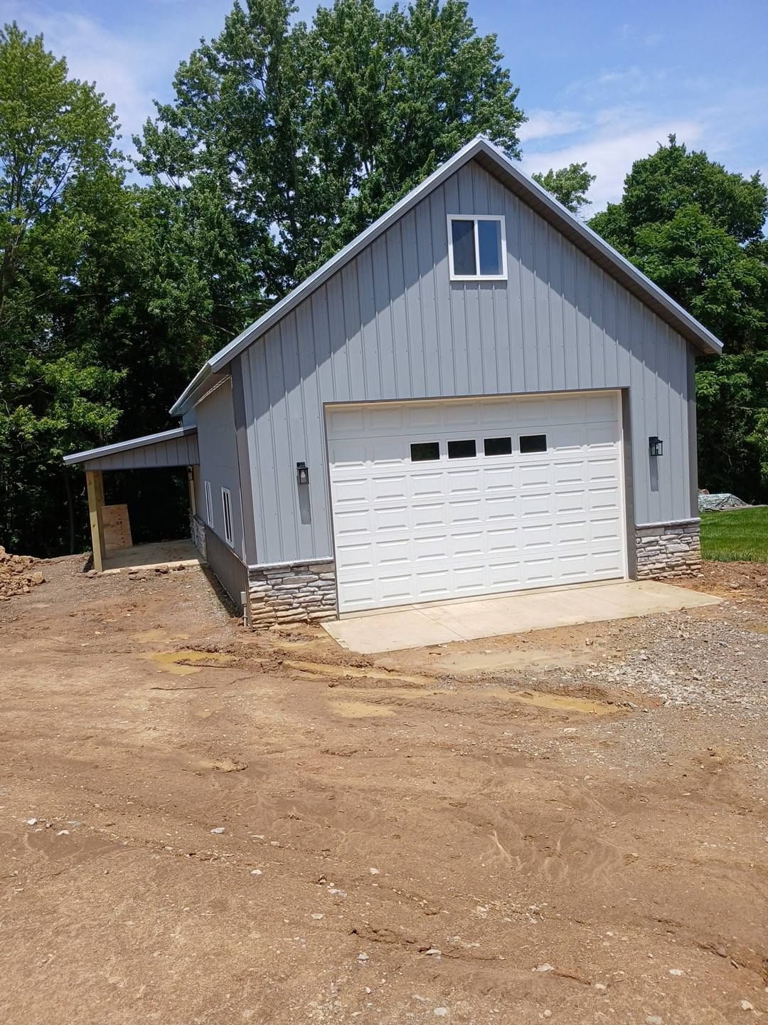 Gray barn with white garage door, a stone base, and a small covered side area.