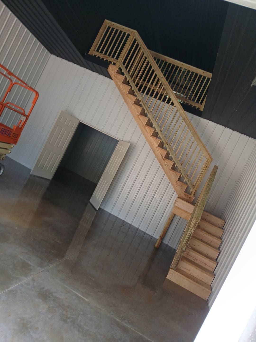 Staircase with wooden steps and railing leading to a balcony in an open-plan space.