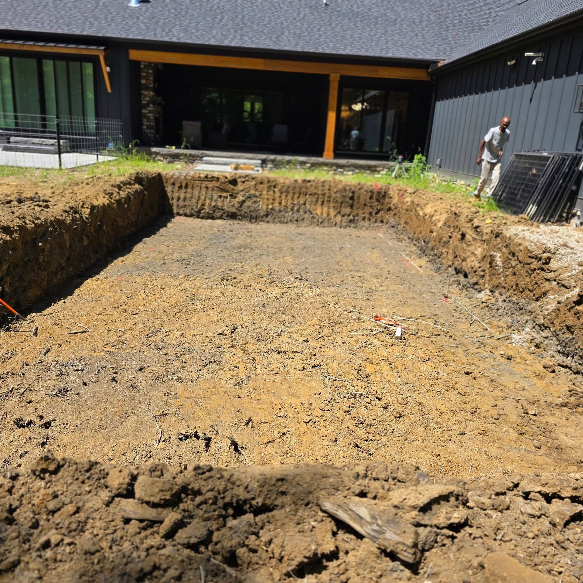Excavated rectangular pool foundation in a backyard, with a man standing nearby.