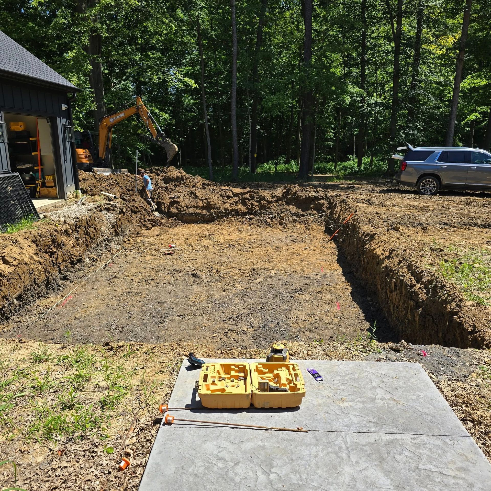 Construction site: Excavation for a pool in a backyard. A backhoe, car, and equipment are present.