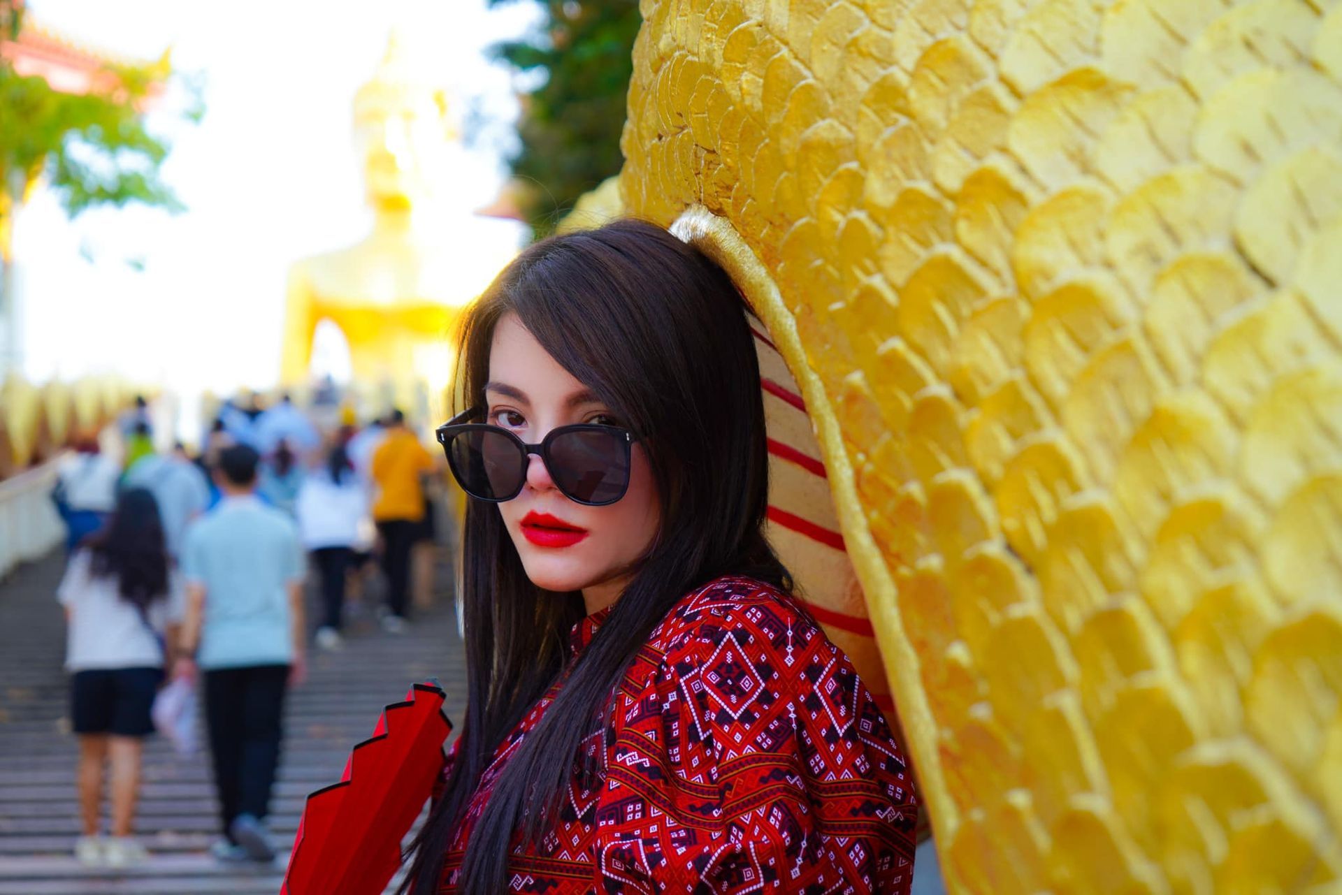 A woman wearing sunglasses and a red dress is standing in front of a large statue.