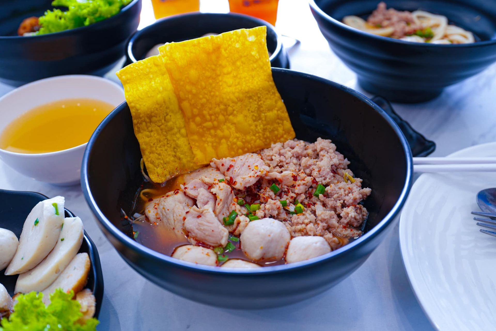 A bowl of food with fishballs and noodles on a table.
