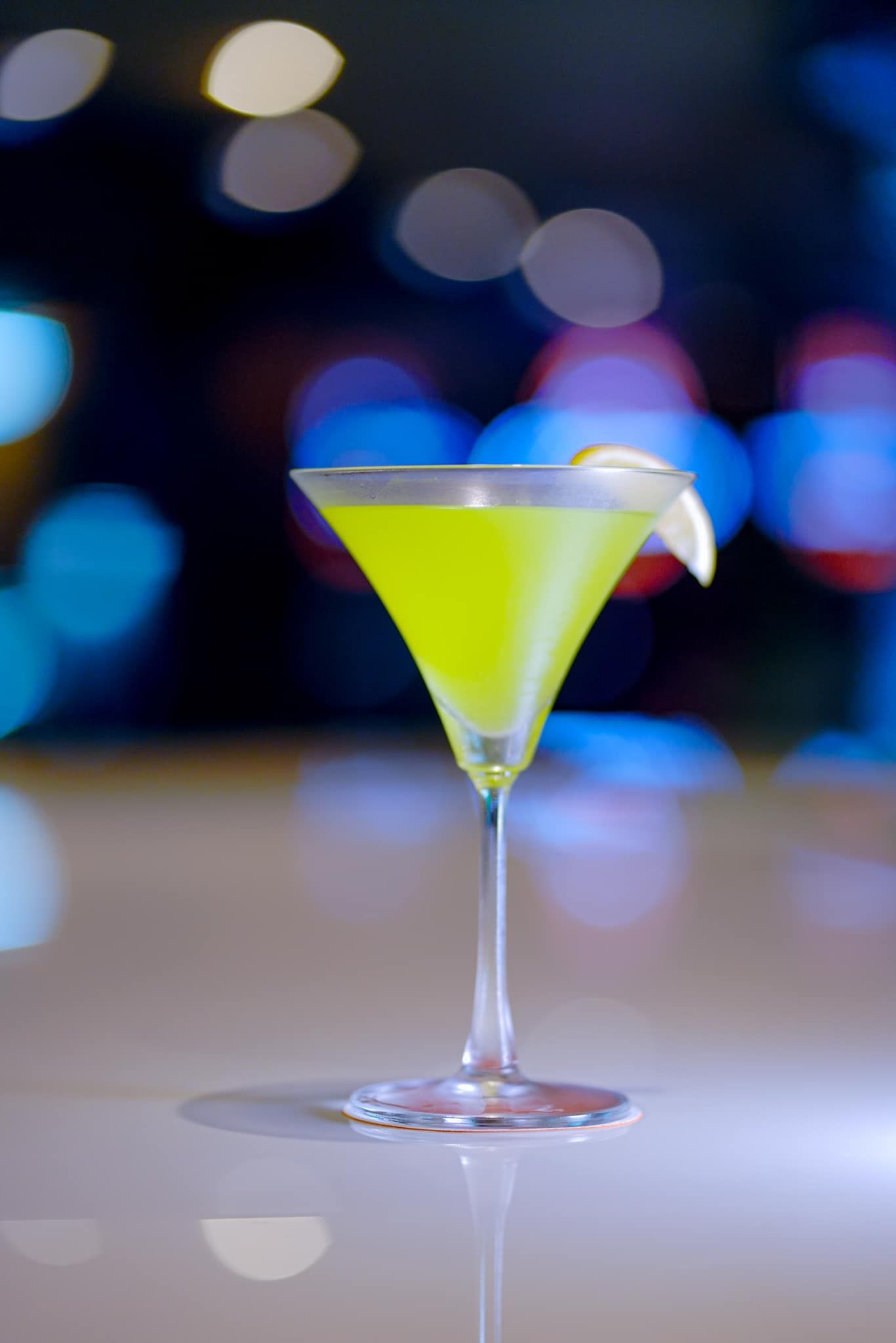 A green cocktail in a martini glass on a table.