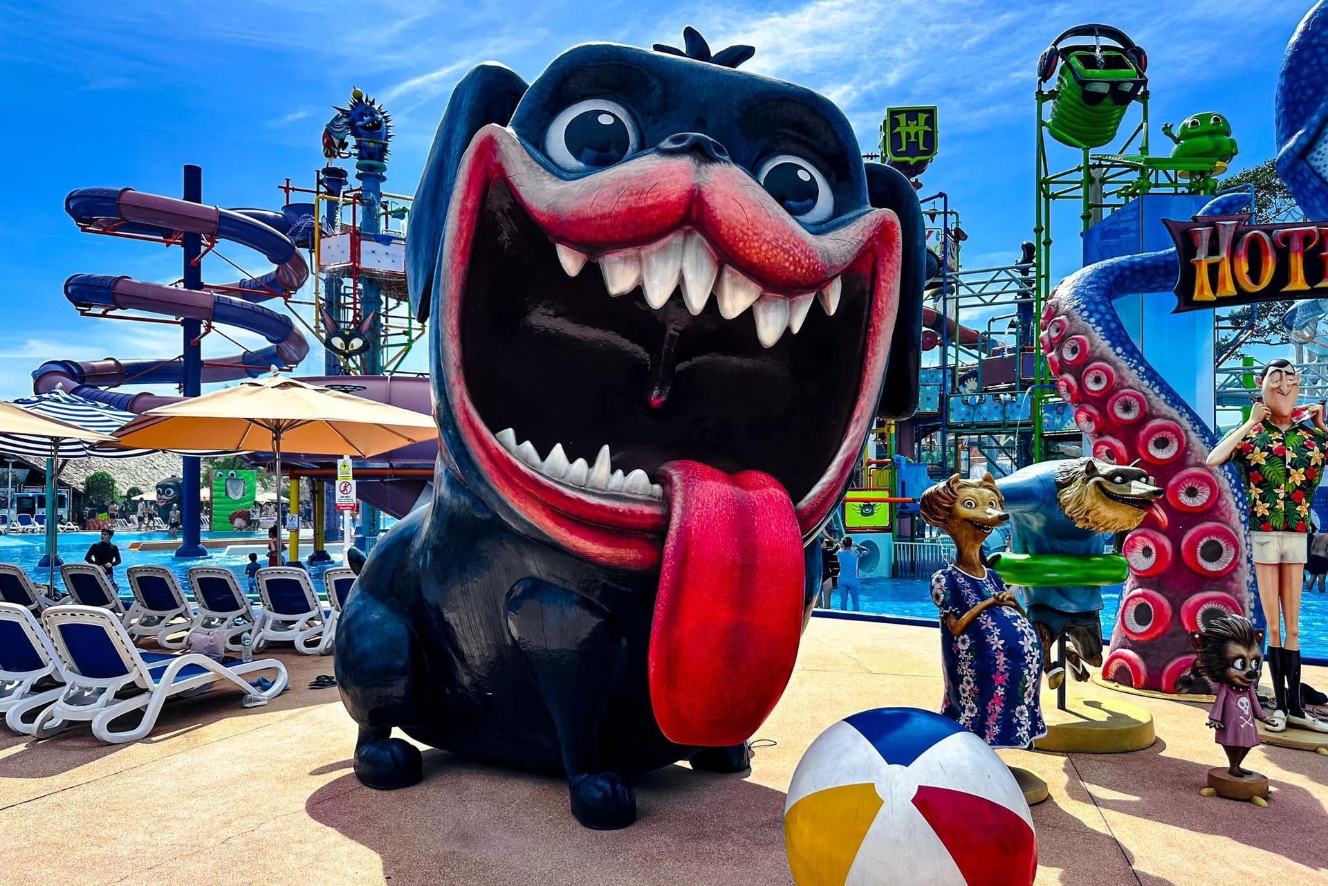 A statue of a dog with its tongue hanging out is at a water park.