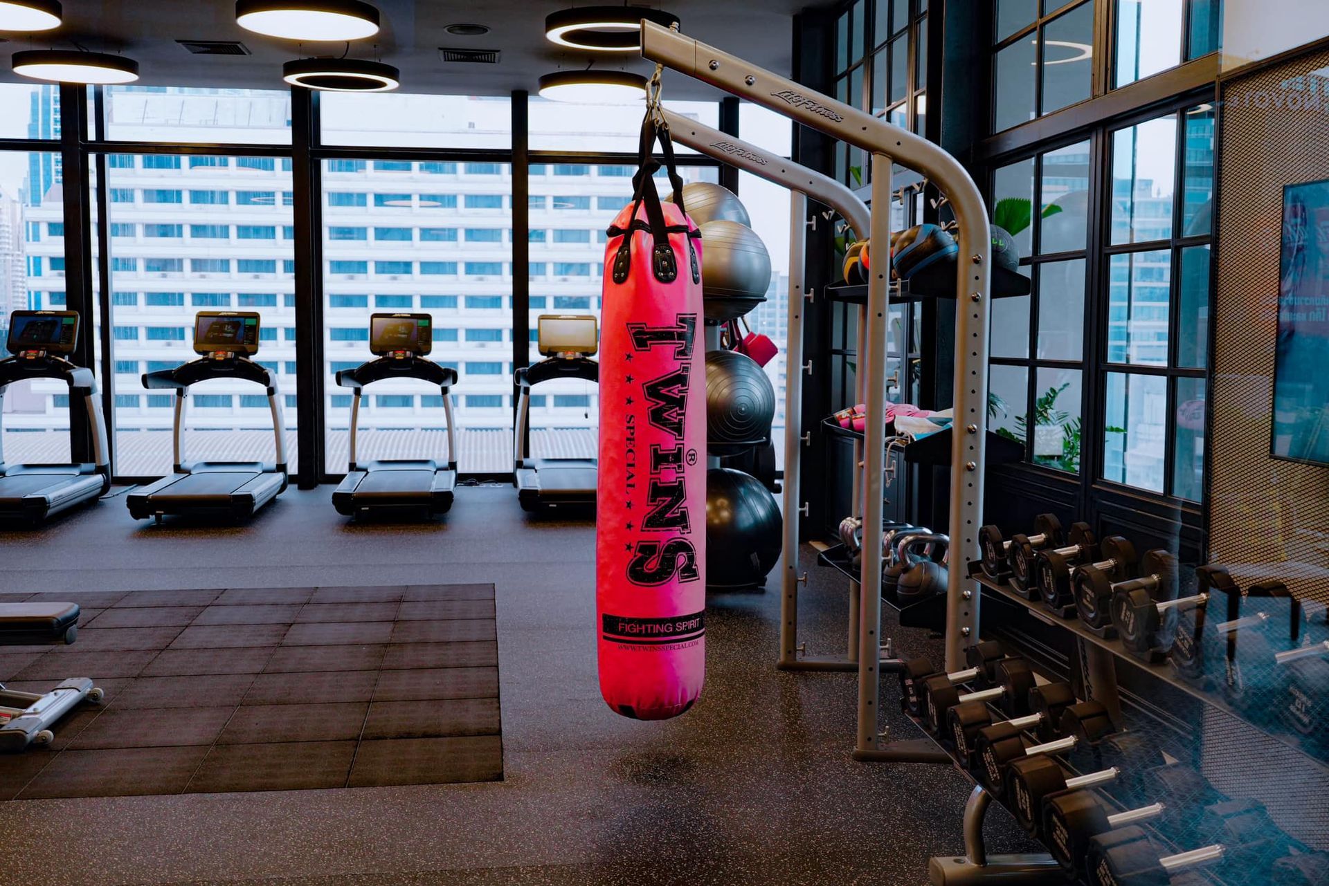 A pink boxing bag is hanging from a rack in a gym.