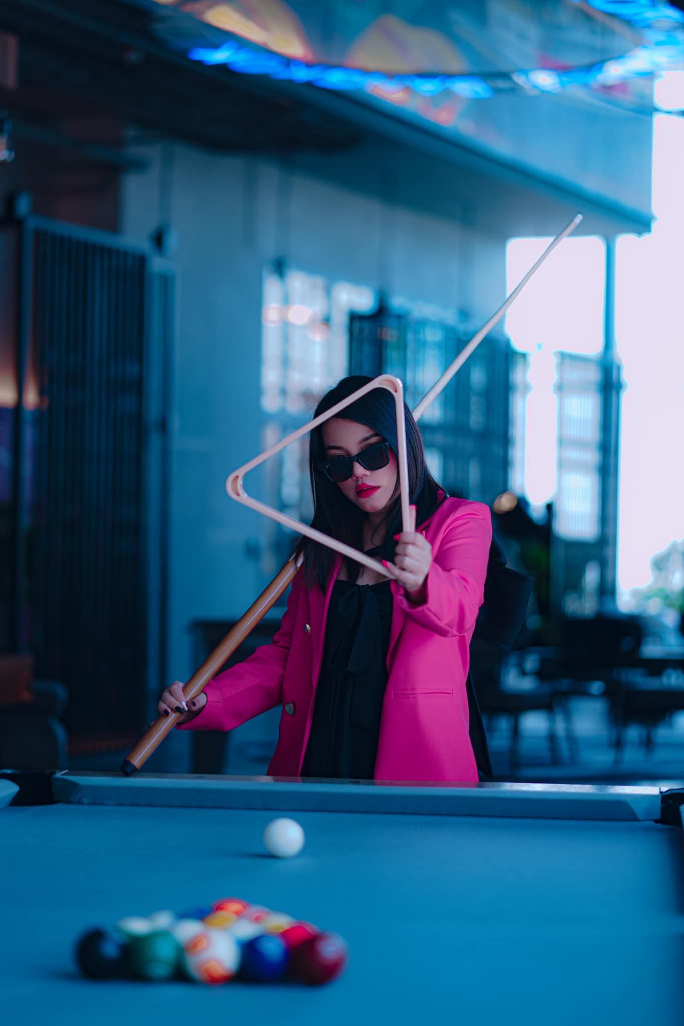A woman in a pink jacket is playing pool on a pool table.