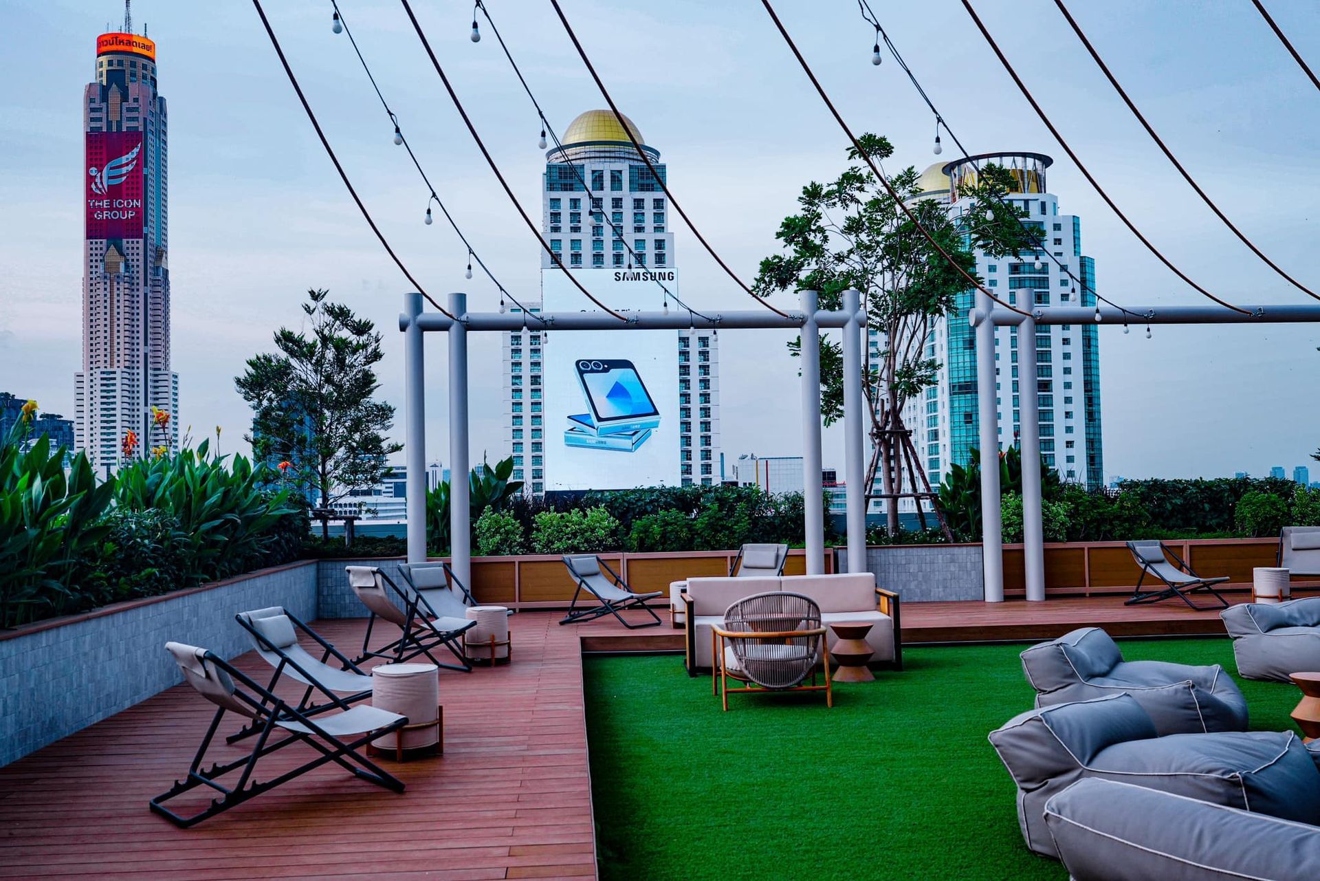 A rooftop garden with chairs , a couch , and a swing in Moxy Bangkok Ratchaprasong hotel..