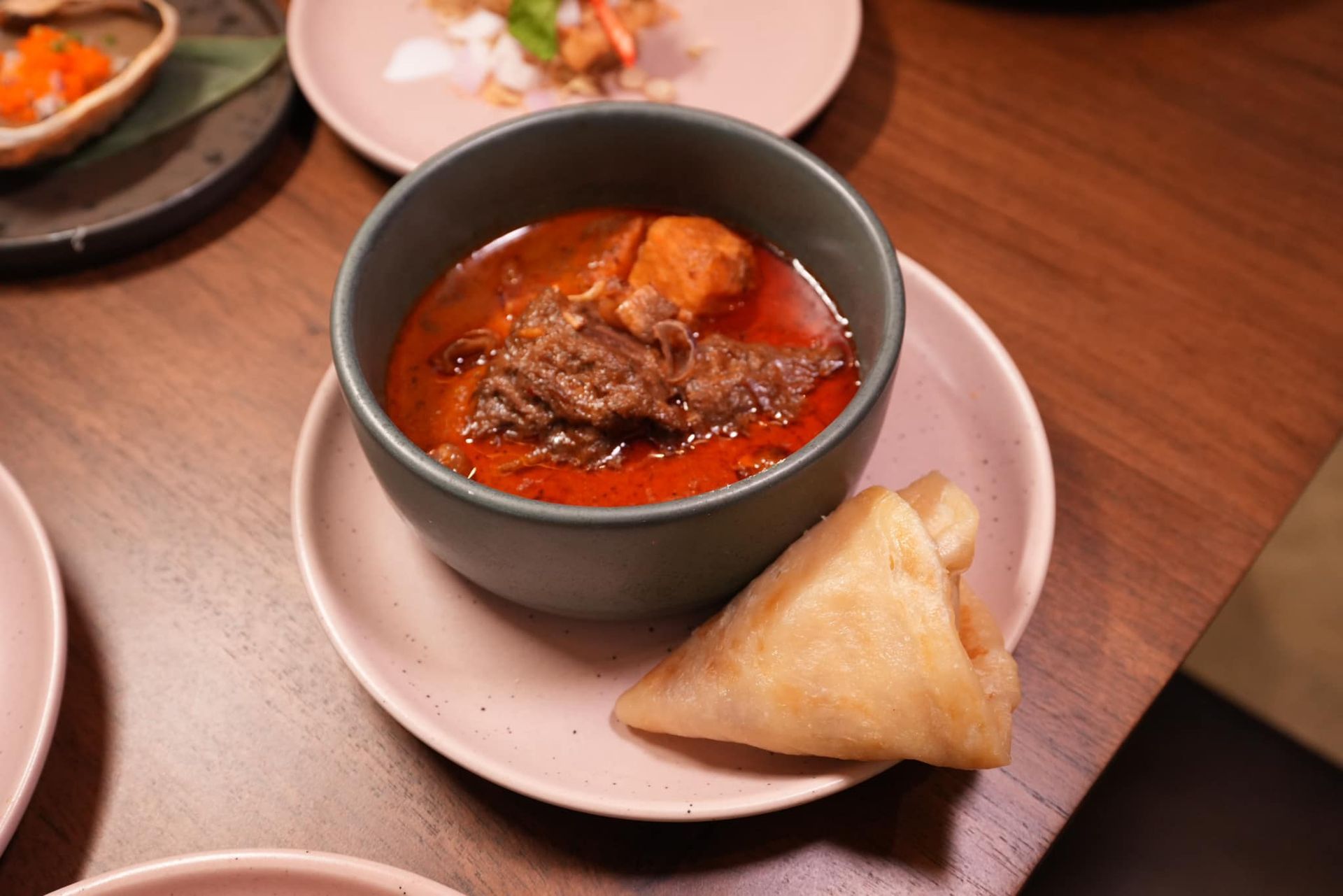 A bowl of soup and a piece of food on a plate on a table.