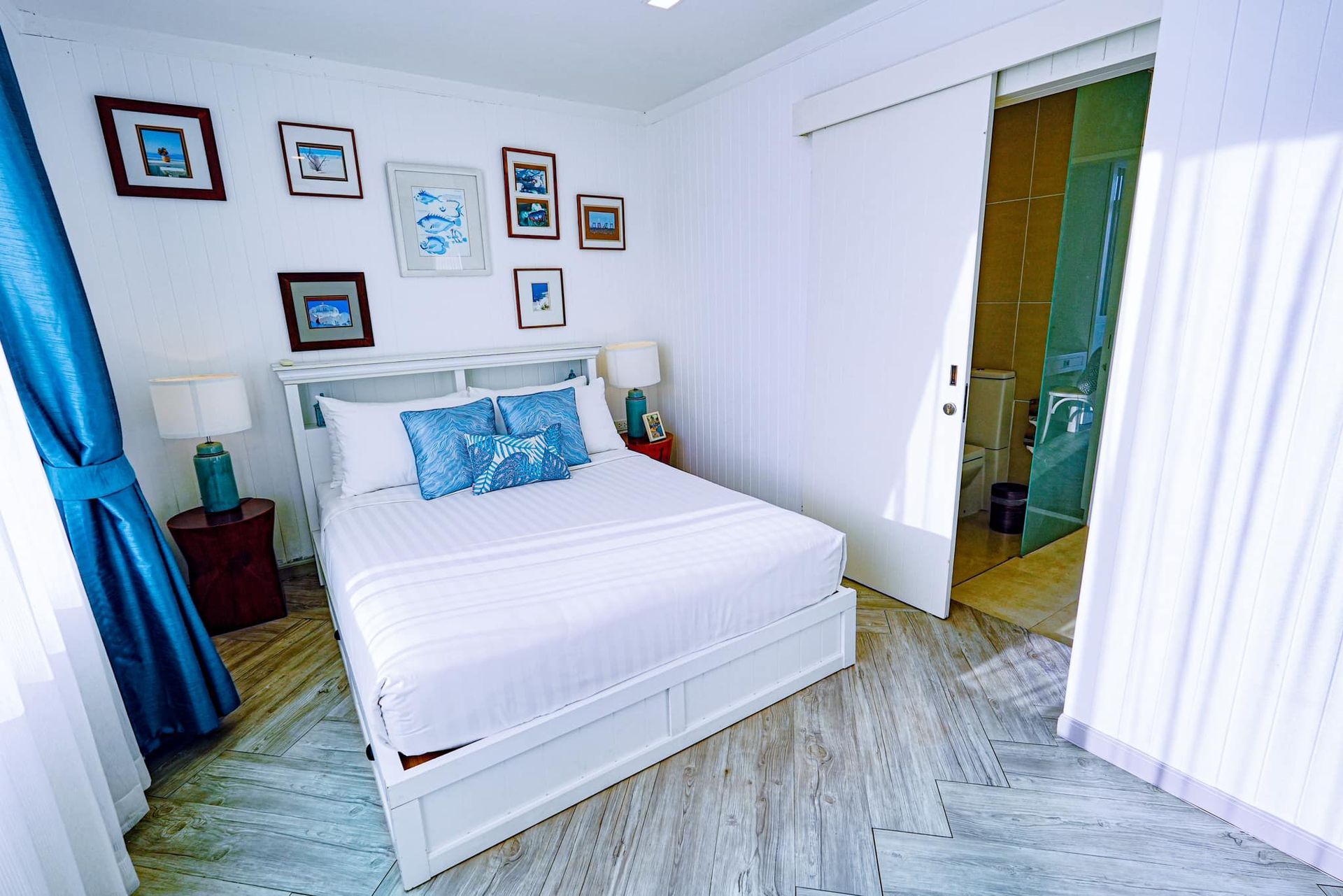 A bedroom with a bed , lamps , curtains and a sliding glass door leading to a bathroom.