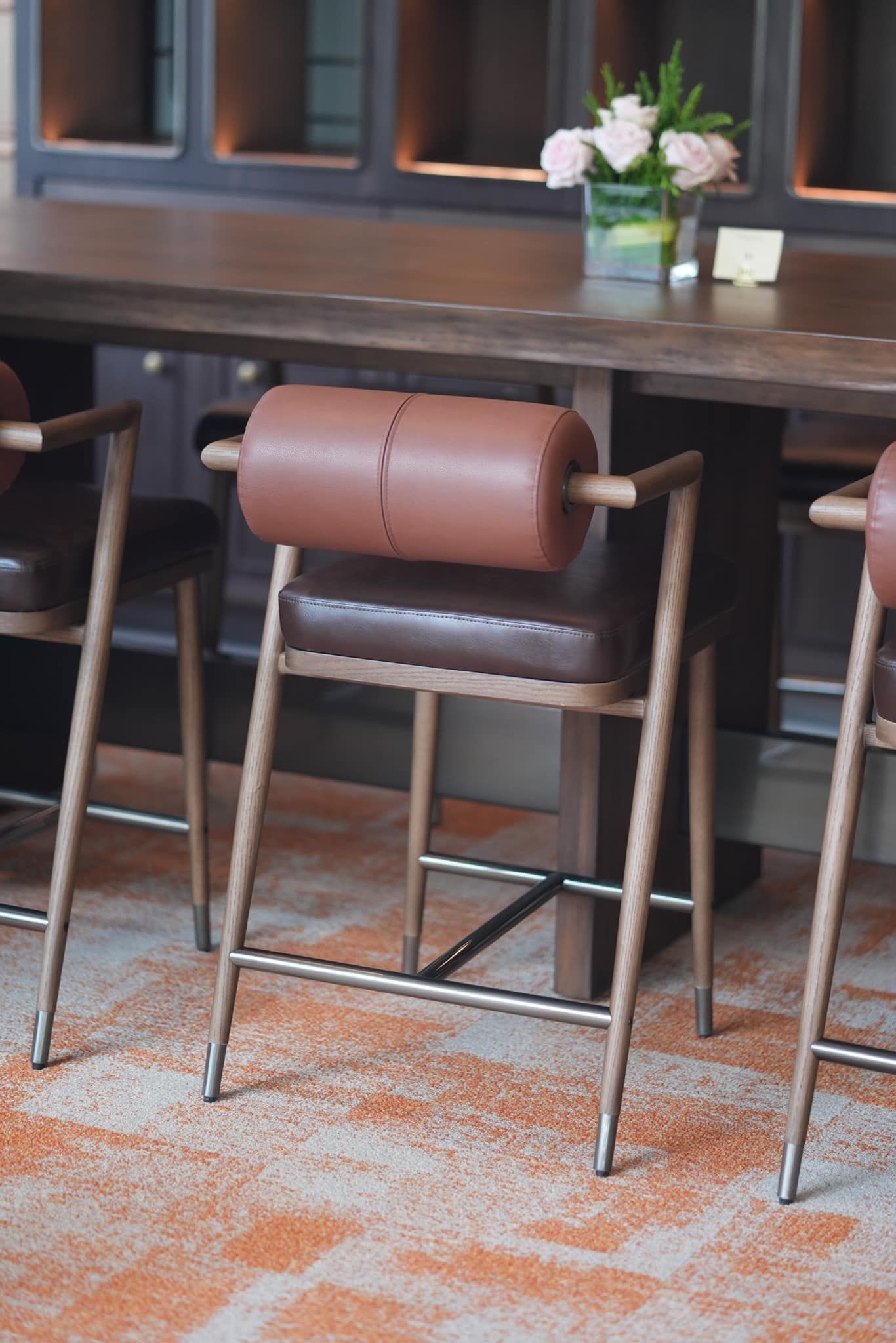 A row of bar stools are sitting next to a table with a vase of flowers on it.