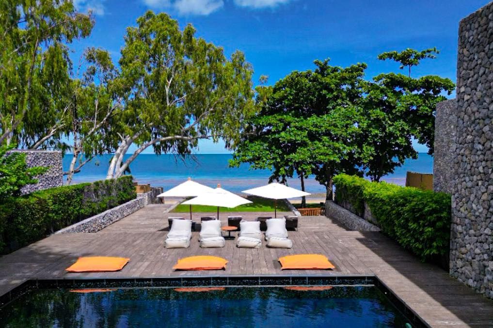 A large swimming pool surrounded by chairs and umbrellas with a view of the ocean.