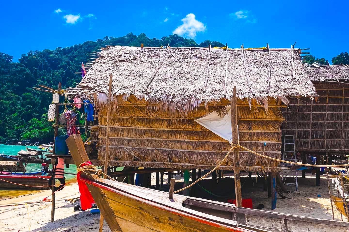 A boat is parked in front of a hut with a thatched roof on a beach.