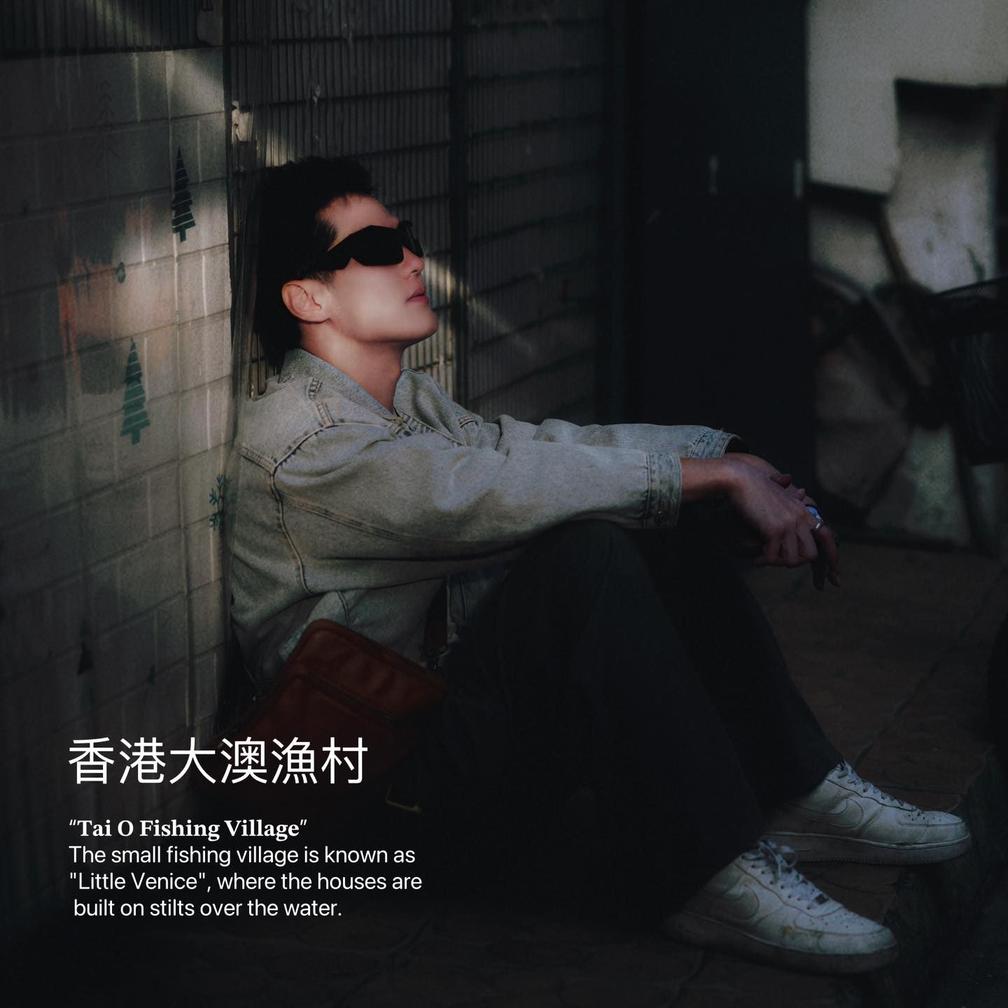 A man wearing sunglasses is leaning against a wall