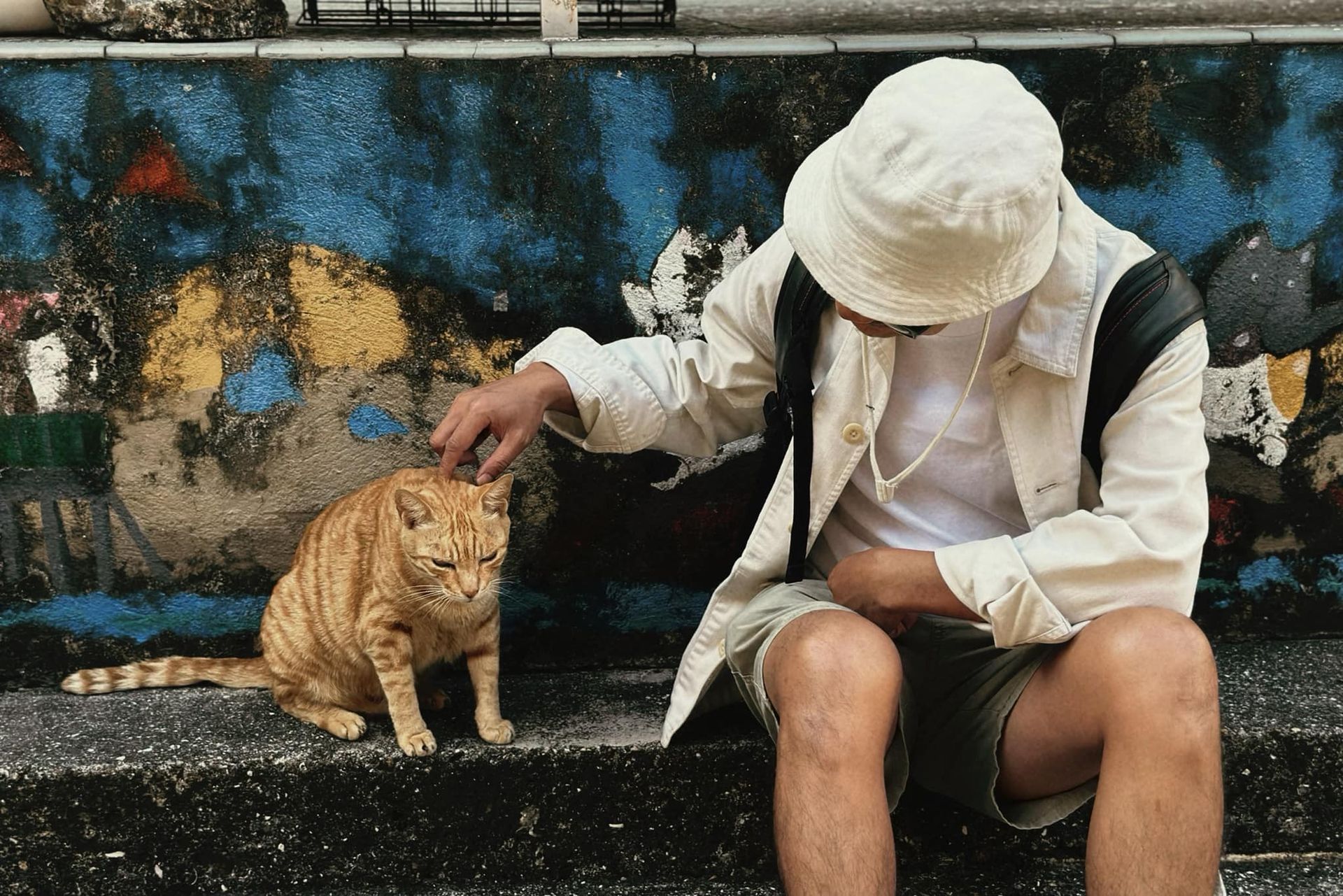 A man is petting a cat while sitting on steps.