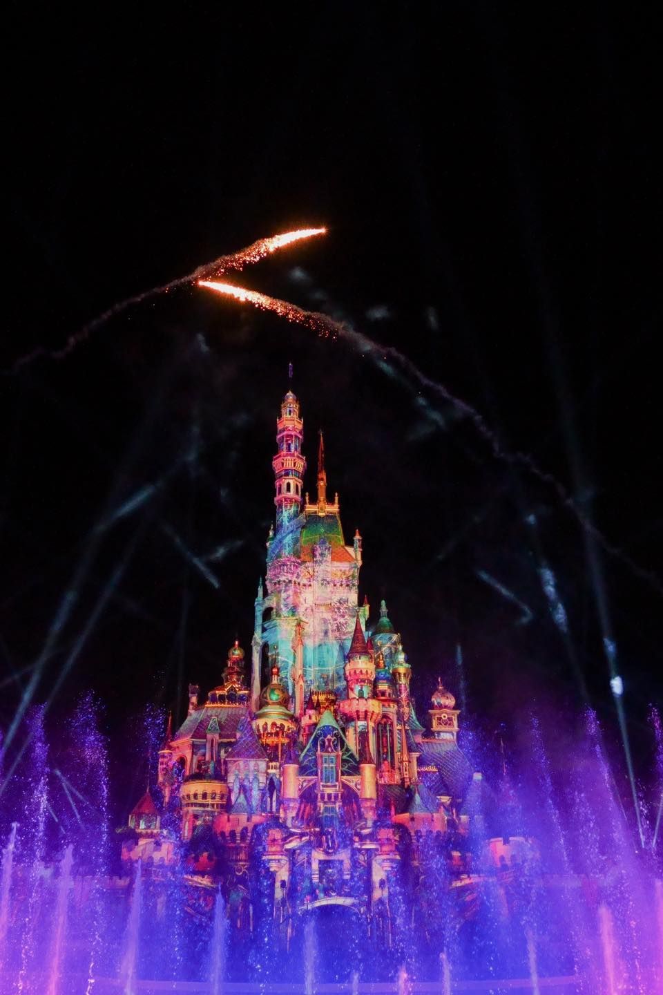A castle is lit up at night with fireworks coming out of it.