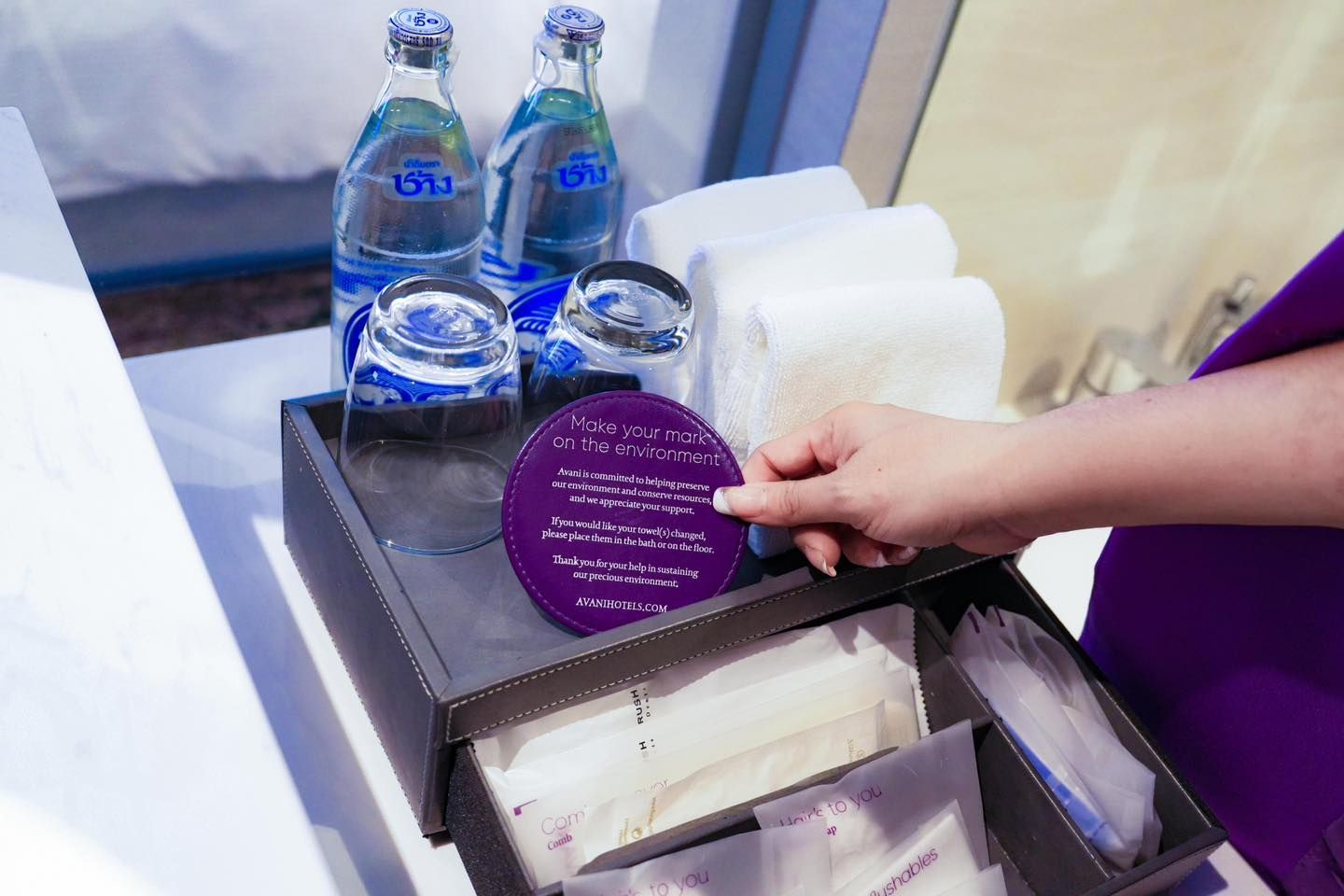 A person is holding a tray with bottles of water and towels on it.