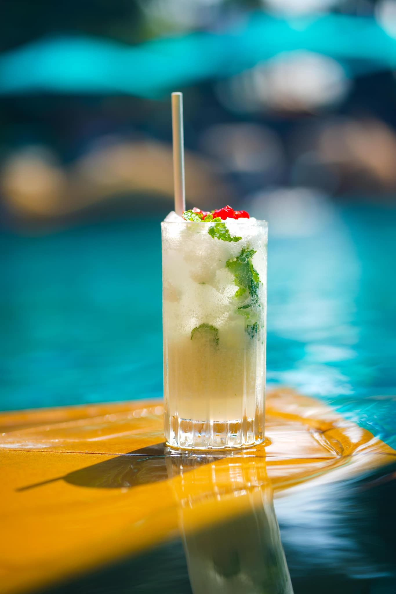 A close up of a drink with a straw on a table next to a pool.