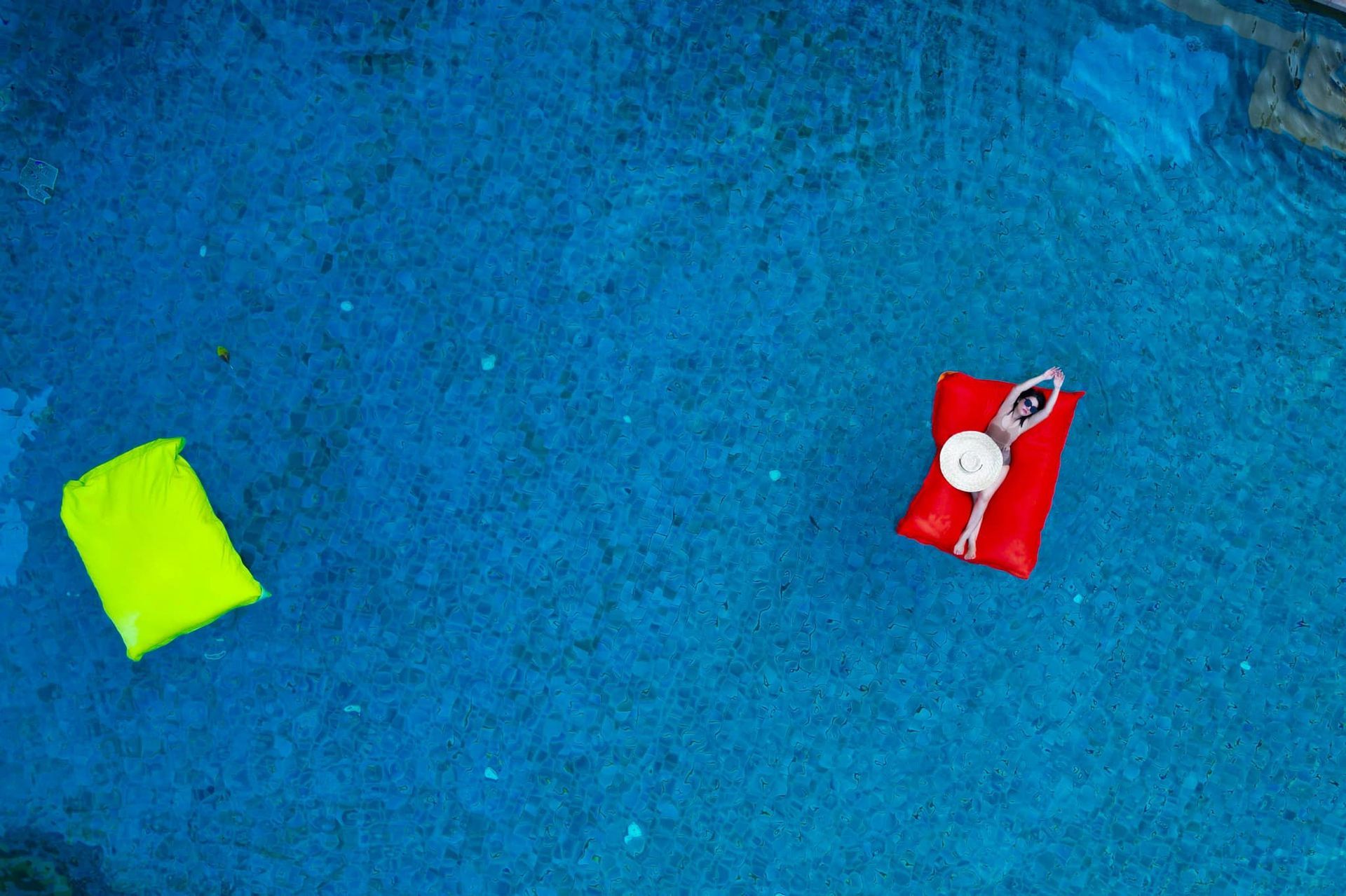 A woman is floating on a red raft in a swimming pool.