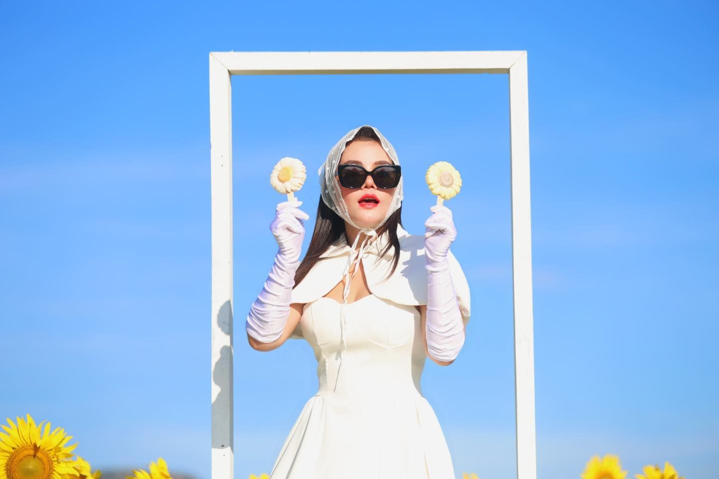 A woman in a white dress and gloves is holding two lollipops.