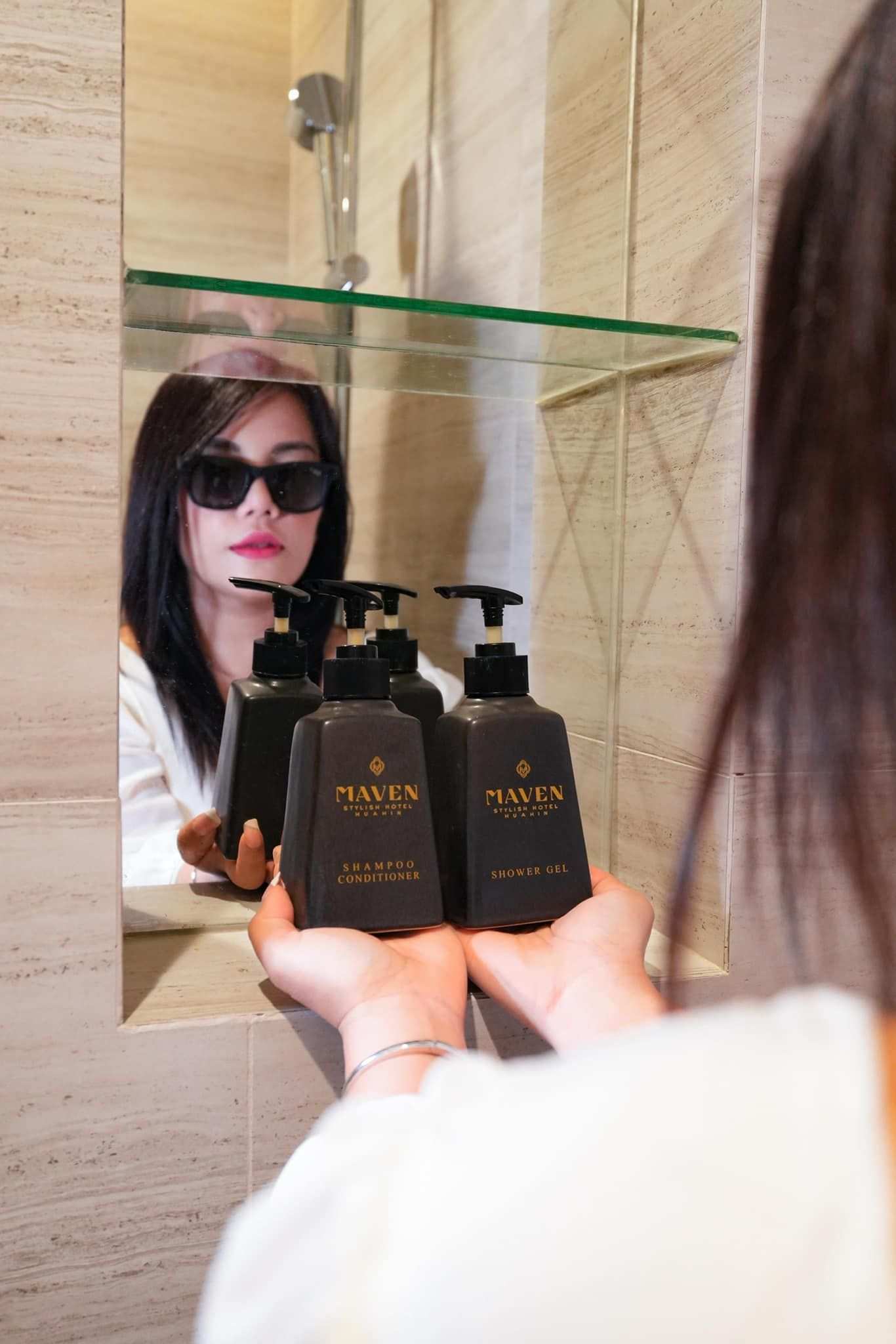 A woman is holding a bottle of shampoo in front of a mirror.