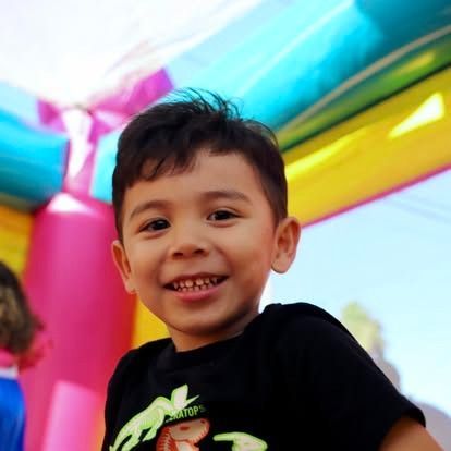 A smiling child in a black t-shirt posing in front of a colorful, bright inflatable bounce house.