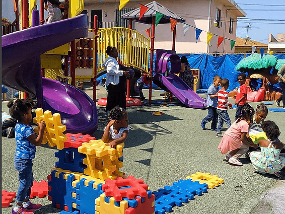 Children play with colorful building blocks in an outdoor playground with slides and a climbing structure.