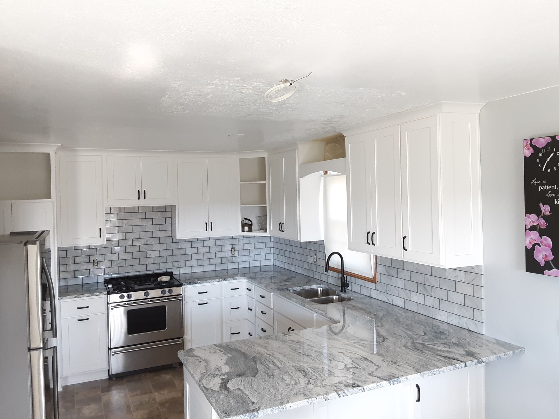 White kitchen with granite countertops, stainless steel appliances, and gray backsplash.