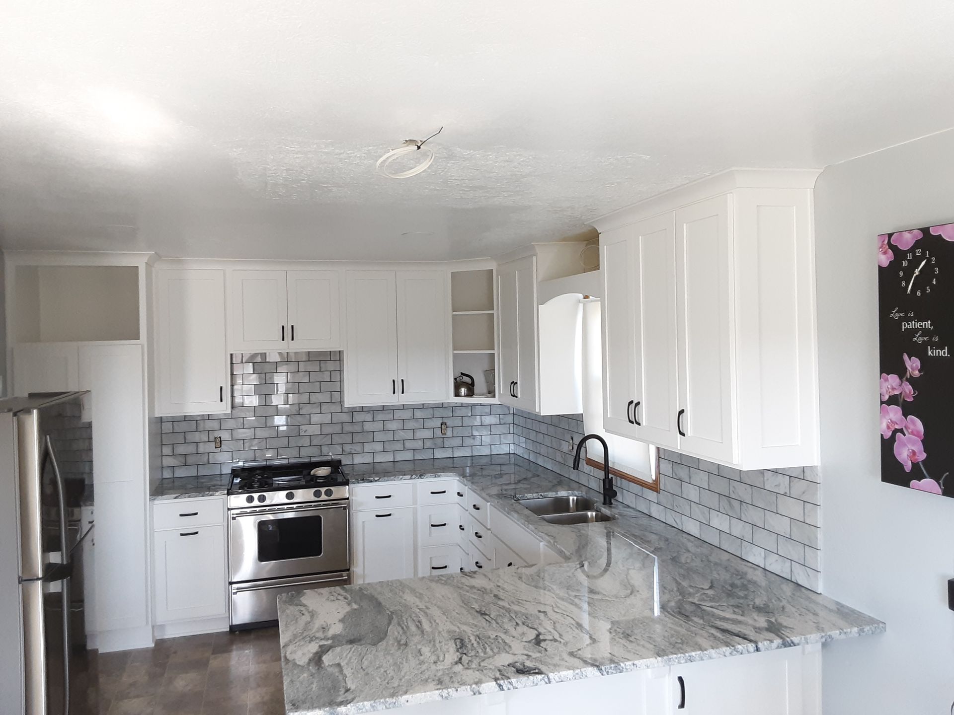 White kitchen with granite countertops, stainless steel appliances, and gray tile backsplash.